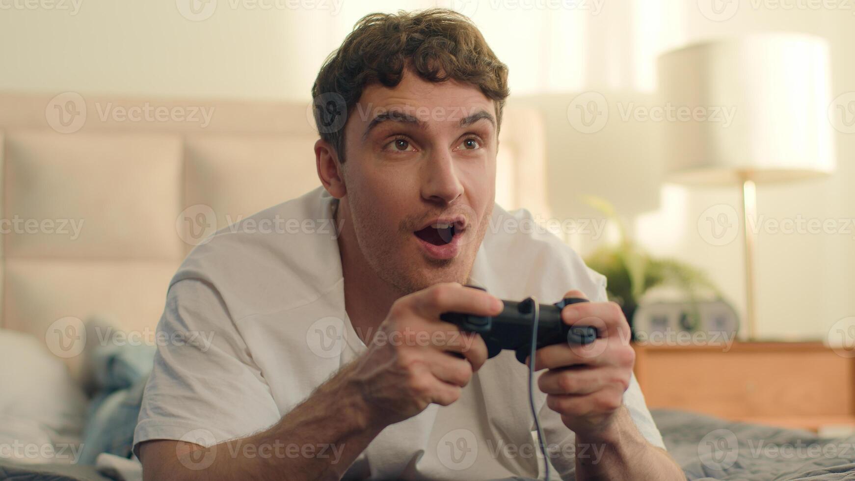 Excited Caucasian man male guy playing console joystick game entertainment laughter smiling virtual winner online competition web bedroom enjoyment pastime electronic control technology cyber photo