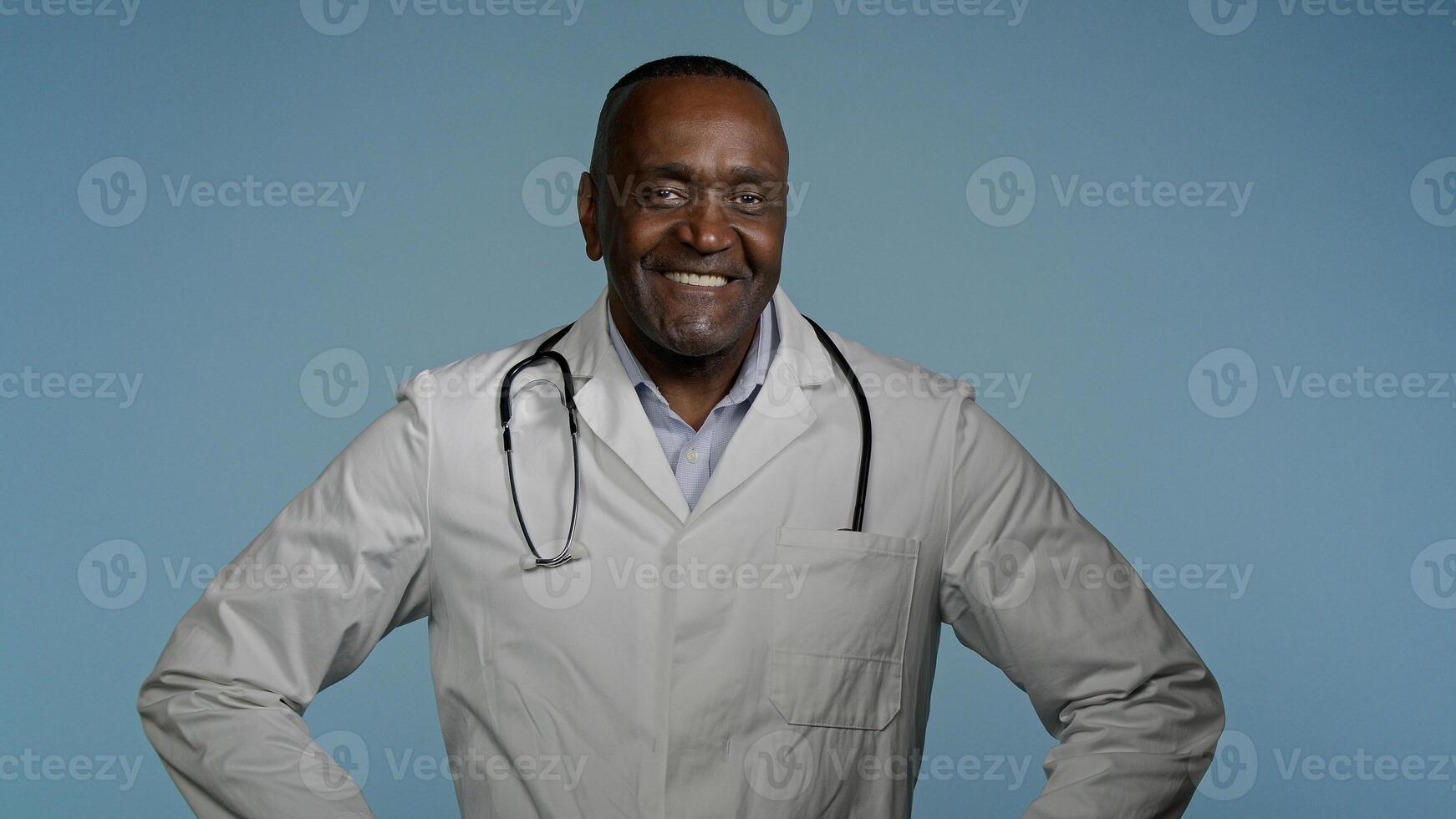 Smiling happy confident african american man professional physician male doctor successful ethnic medical worker clinic surgeon posing in studio blue background looking at camera healthcare medicine photo