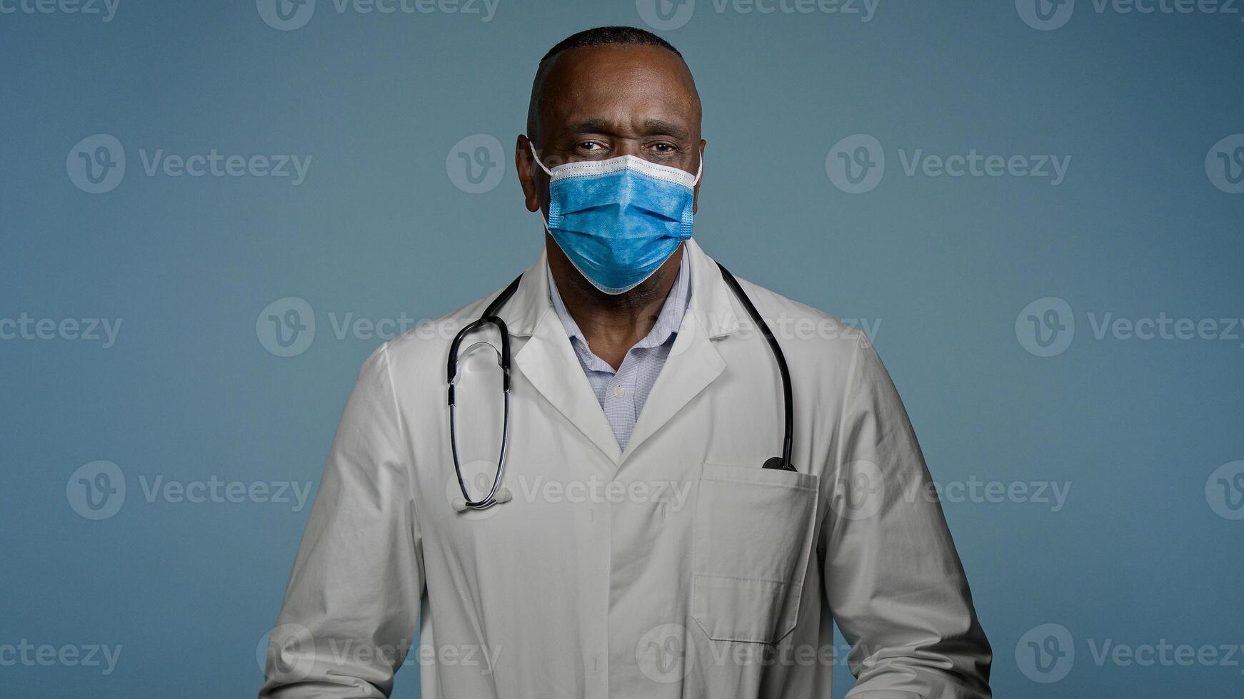 Close-up mature male doctor surgeon in protective mask looks at camera man experienced hospital worker posing in studio on gray background advertising professional specialized medical service medicare photo