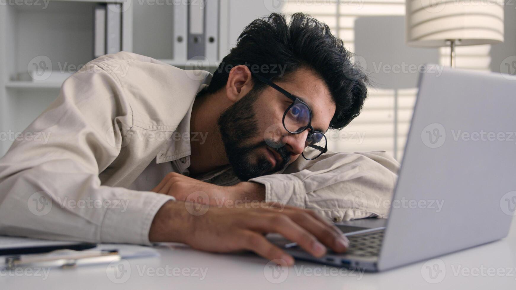 Lazy weary sleepy male manager tired exhausted Arabian Indian businessman employee working computer boring remote job man fall sleep on desktop napping in office overwork fatigue no energy sleeping photo