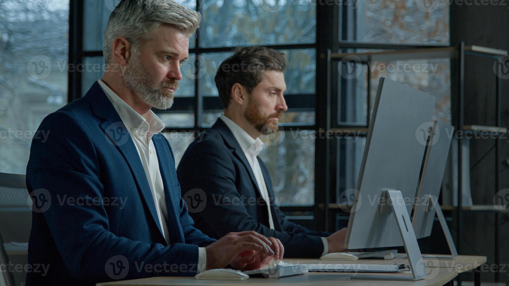 Focused professional managers working with computers on project sit in row at desk in office caucasian adult business men businessmen corporate employees colleagues work on Internet typing on computer photo