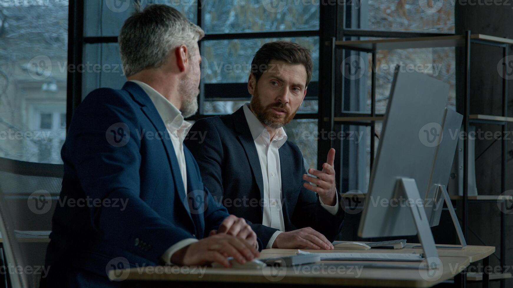 Two Caucasian men professional businessmen work together using computer in office discussing business project check financial data plan colleagues talking about marketing strategy corporate teamwork photo