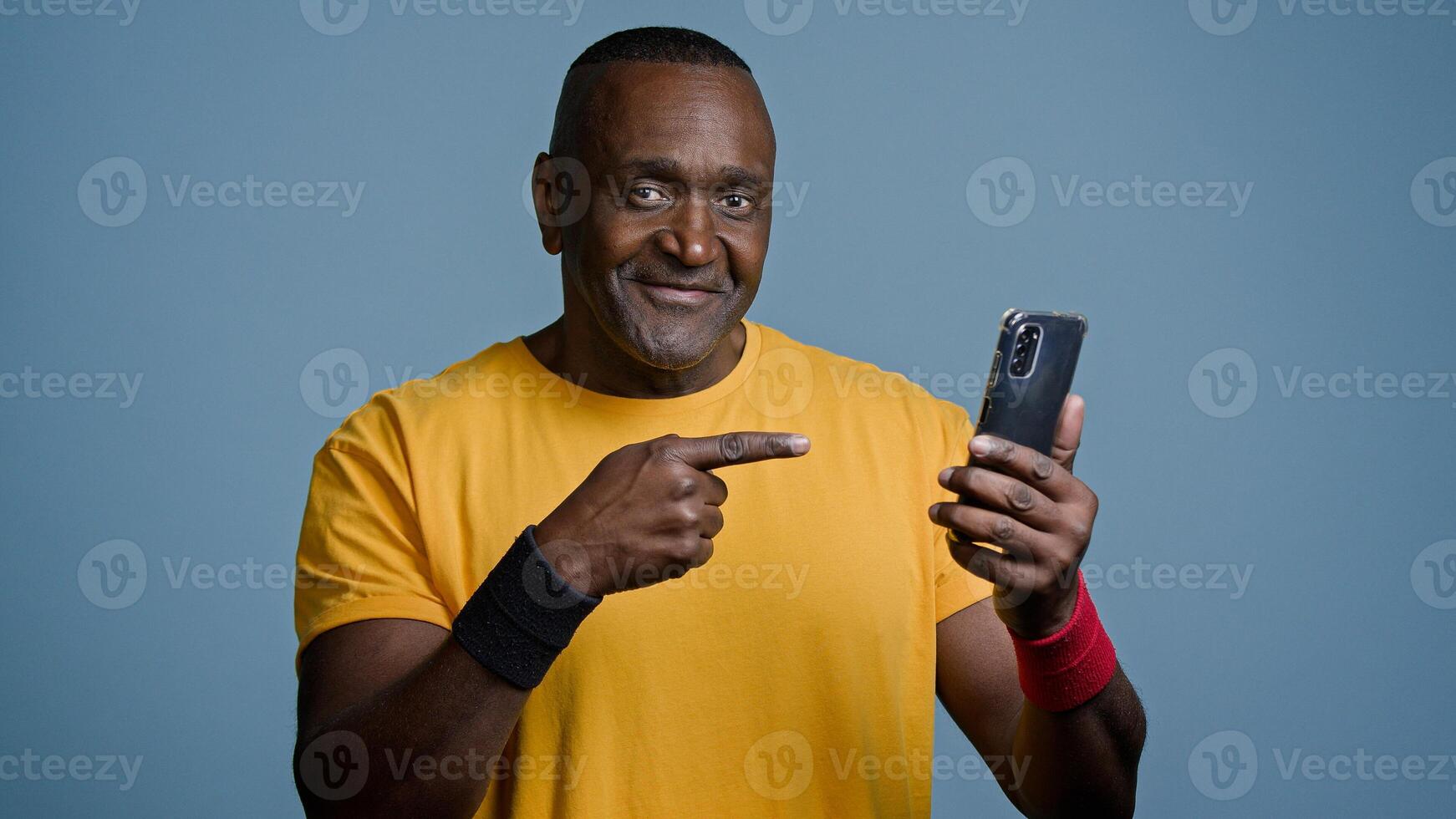 Mature man athlete instructor trainer watching sports training on phone on internet sportsman looking for strength exercise in social network points to smartphone screen nods head in approval photo