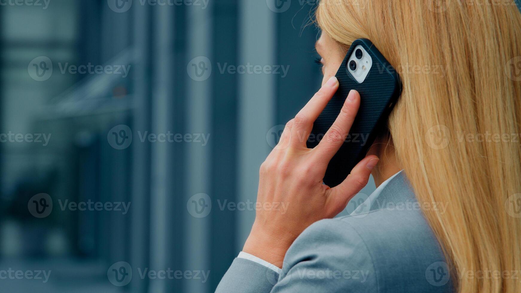Back view close-up blonde caucasian businesswoman talking on mobile phone answering business call remotely communicates with client using smartphone woman leader standing outdoors speaks on telephone photo