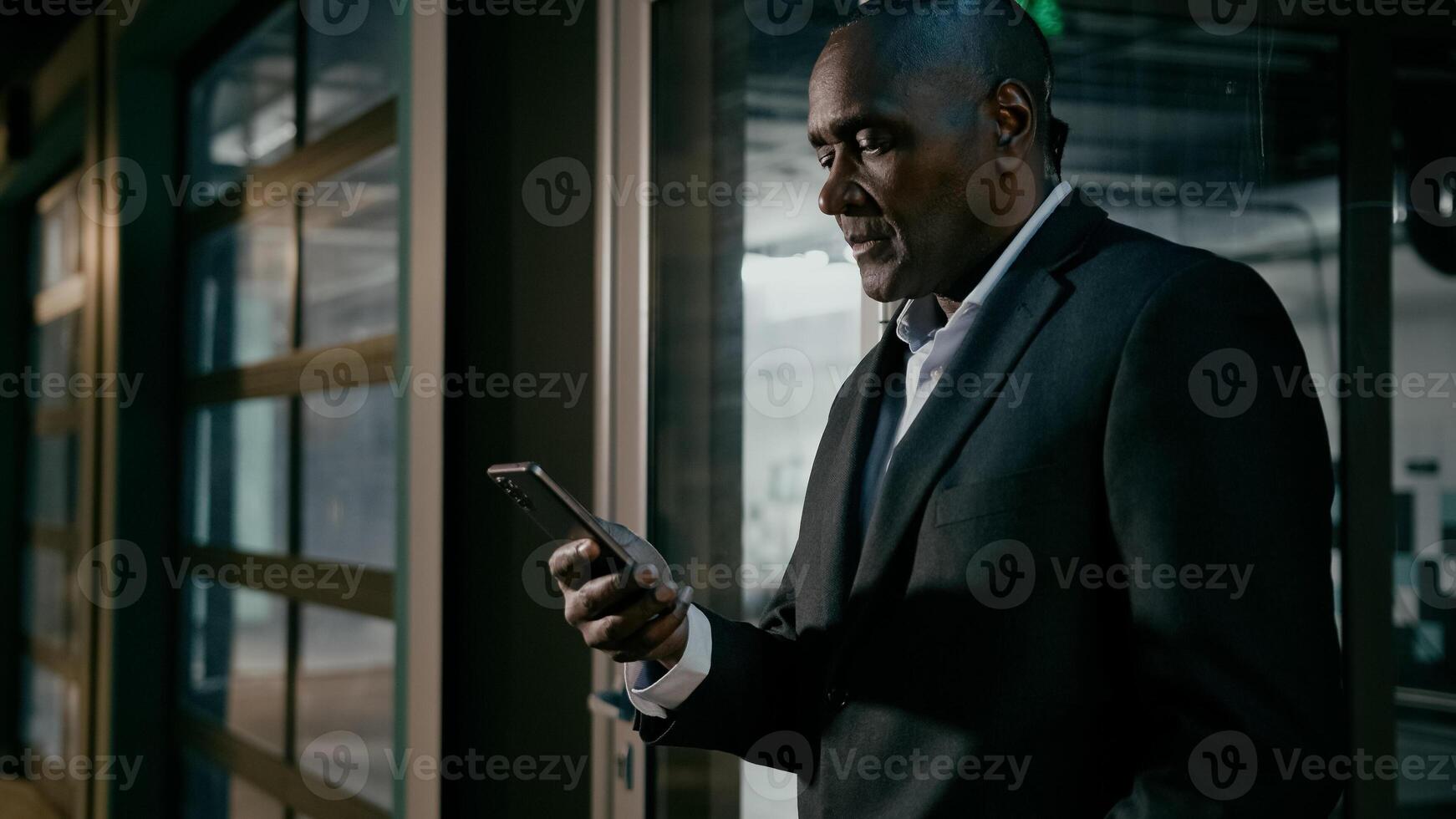 Serious focused businessman holding mobile phone chatting on internet browsing social network mature african man communicate with business client online writing electronic text message uses smartphone photo