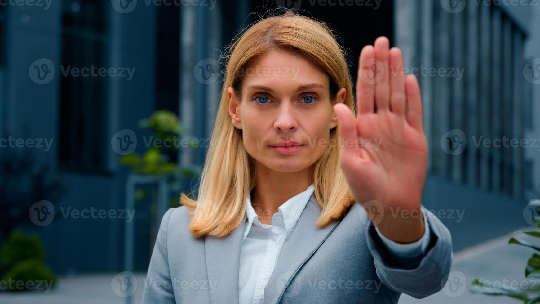 Serious woman standing outdoors looking at camera showing stop gesture holding palm in front confident businesswoman protecting personal boundaries demonstrates prohibition sign keep your distance photo