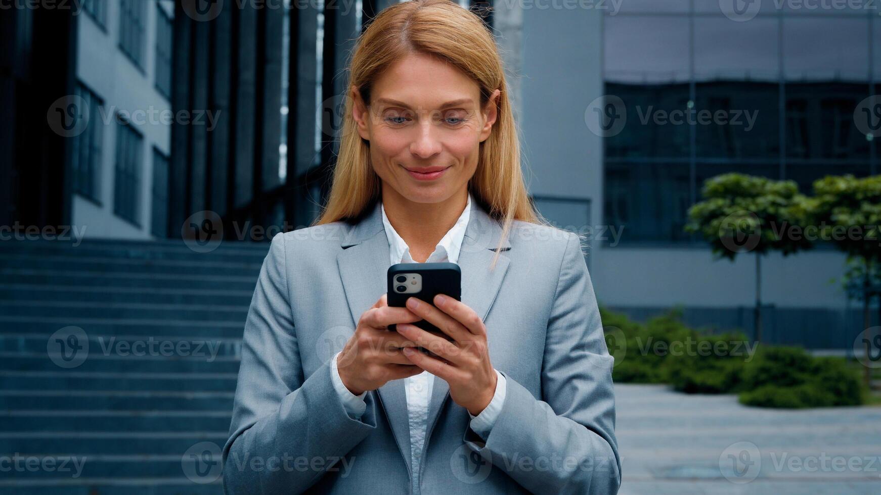 Young woman stand on downtown with phone in hands typing business email answering message in social media smiling businesswoman using mobile application for remote internet communication on smartphone photo