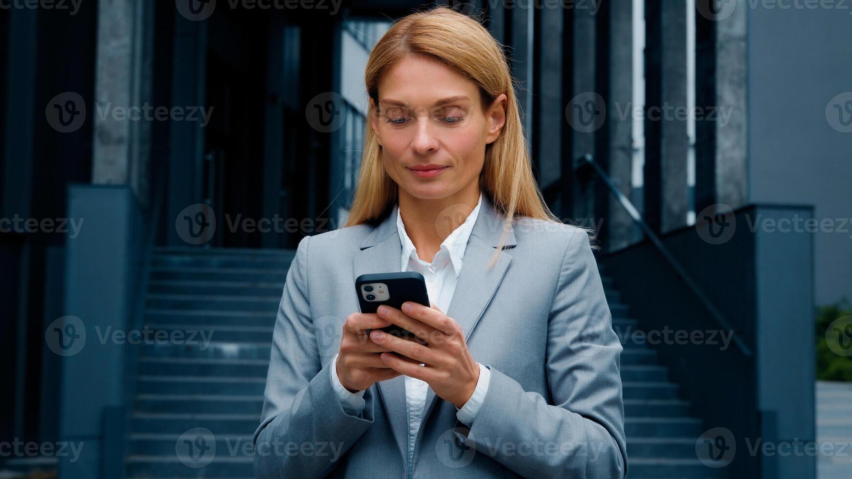 Young woman stand on downtown with phone in hands typing business email answering message in social media smiling businesswoman using mobile application for remote internet communication on smartphone photo