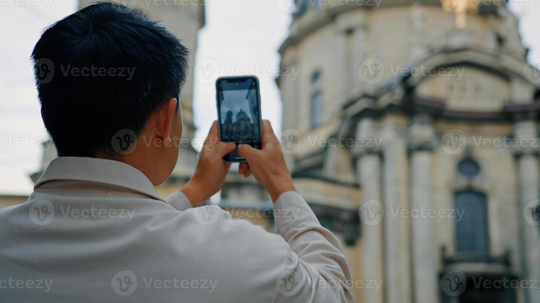 Back view unrecognizable man tourist travels in Europe photographing landmark using camera of mobile phone male blogger traveler holding smartphone taking pictures historical building in city center photo