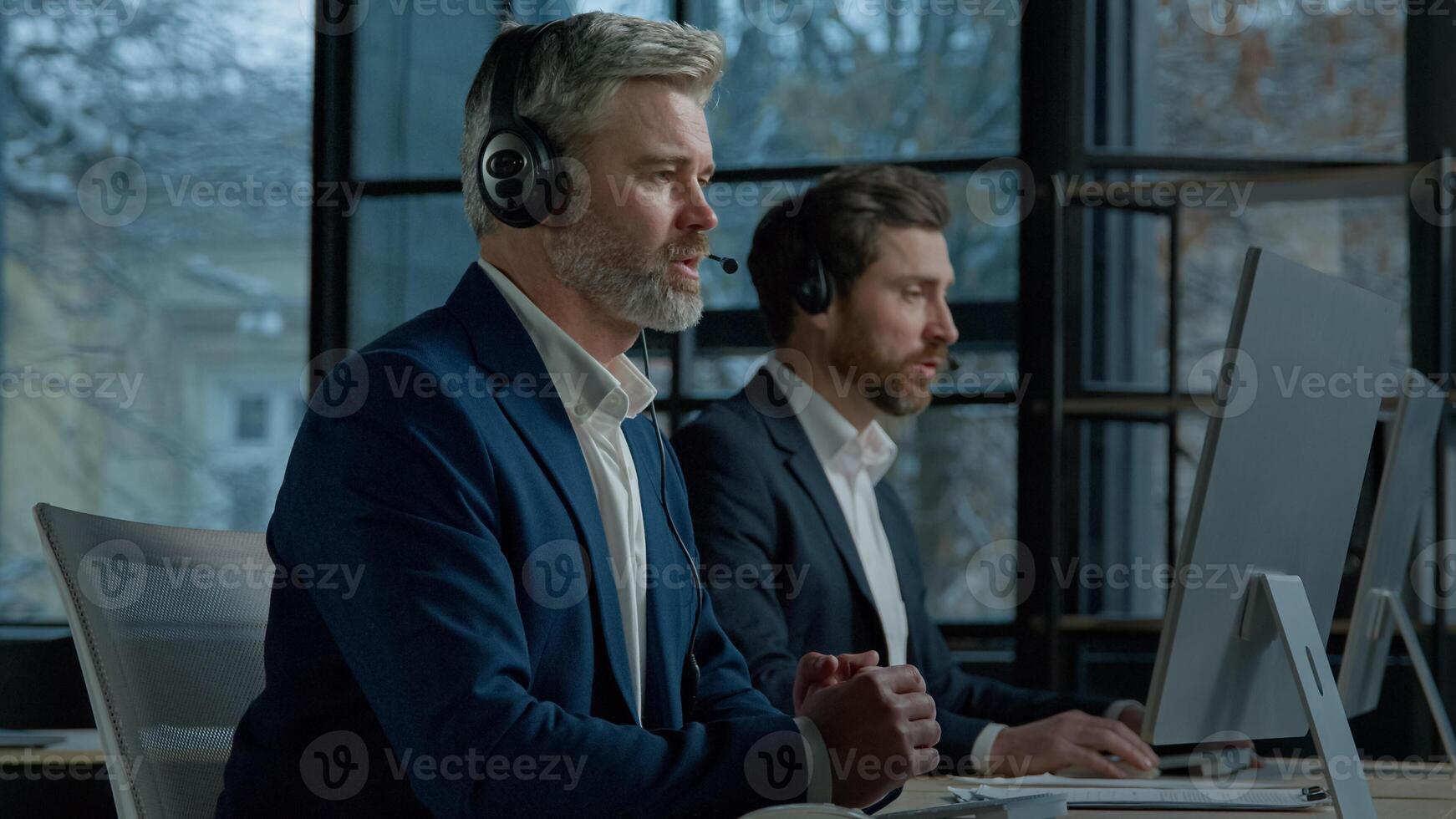Two men call center service operators work in office talk to client using headset on computer concentrated sales agents sell online answering incoming call provide professional support to customers photo