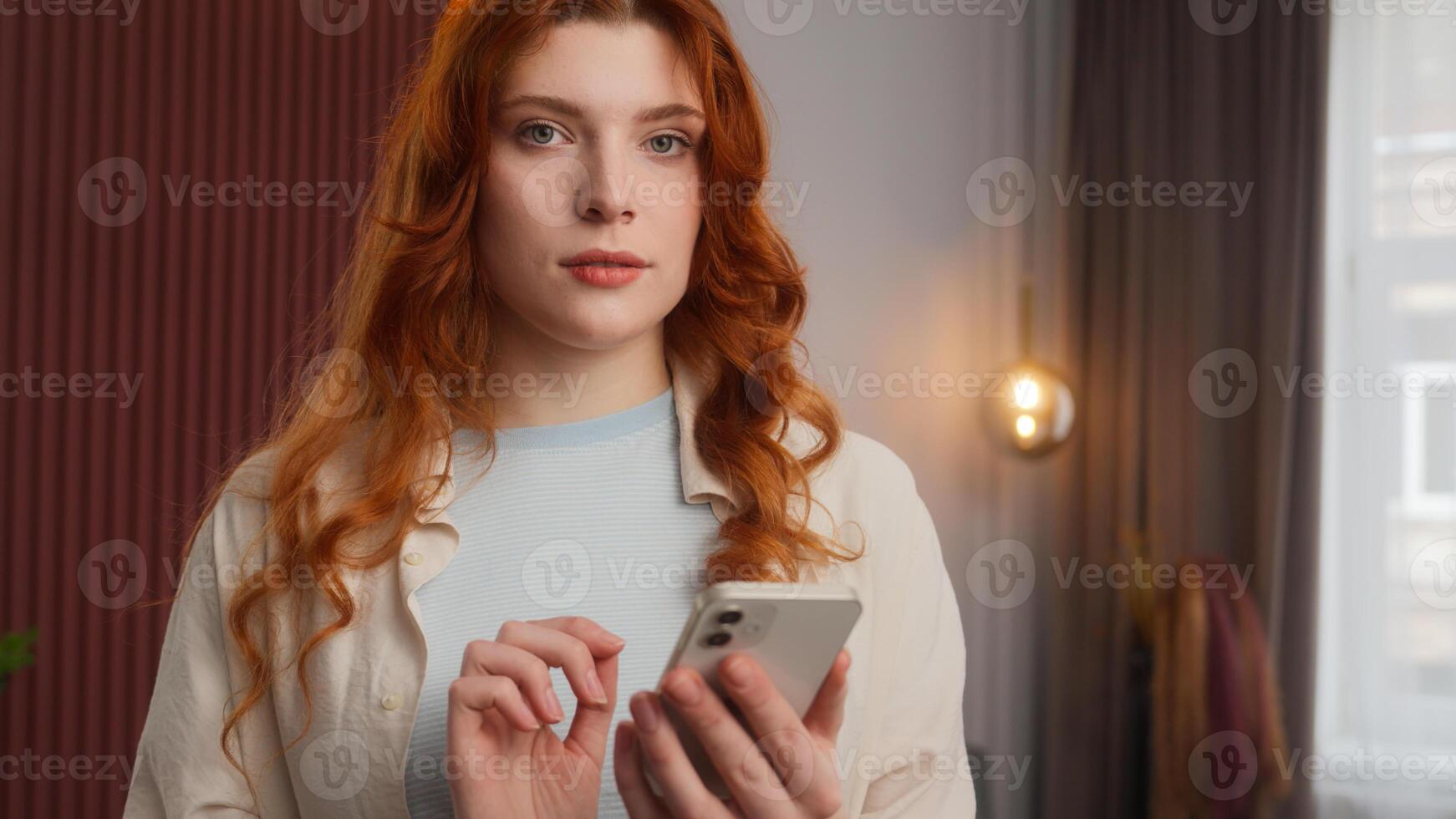 Carefree Caucasian woman girl touch screen using smartphone relaxed lady scrolling digital feed in social media Internet by mobile phone device at home calm female look in camera cyberspace connection photo
