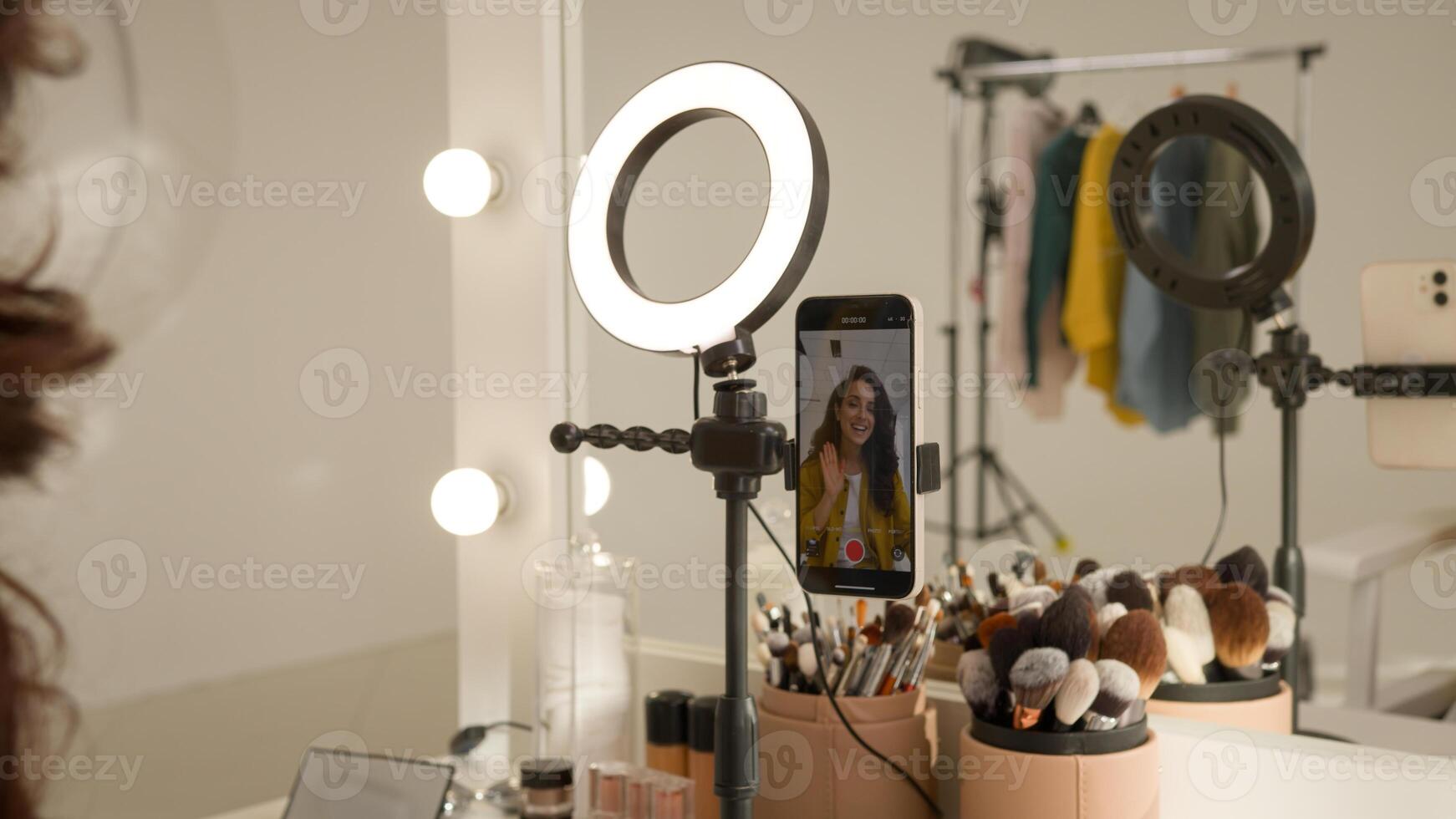 Glad Caucasian woman blogger girl influencer filming mobile phone on stabilizer lamp studio female vlogger streamer talk demonstrating shadow palette do makeup tutorial beauty stream blog mirror photo