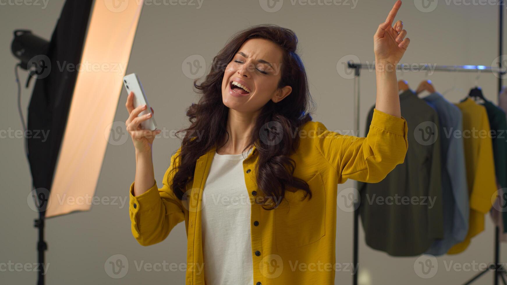 Smiling cheerful Caucasian female woman girl model turning on music mobile smartphone phone dancing fooling around. Positive lady blogger move influencer vlogger singing listen trendy song in studio photo