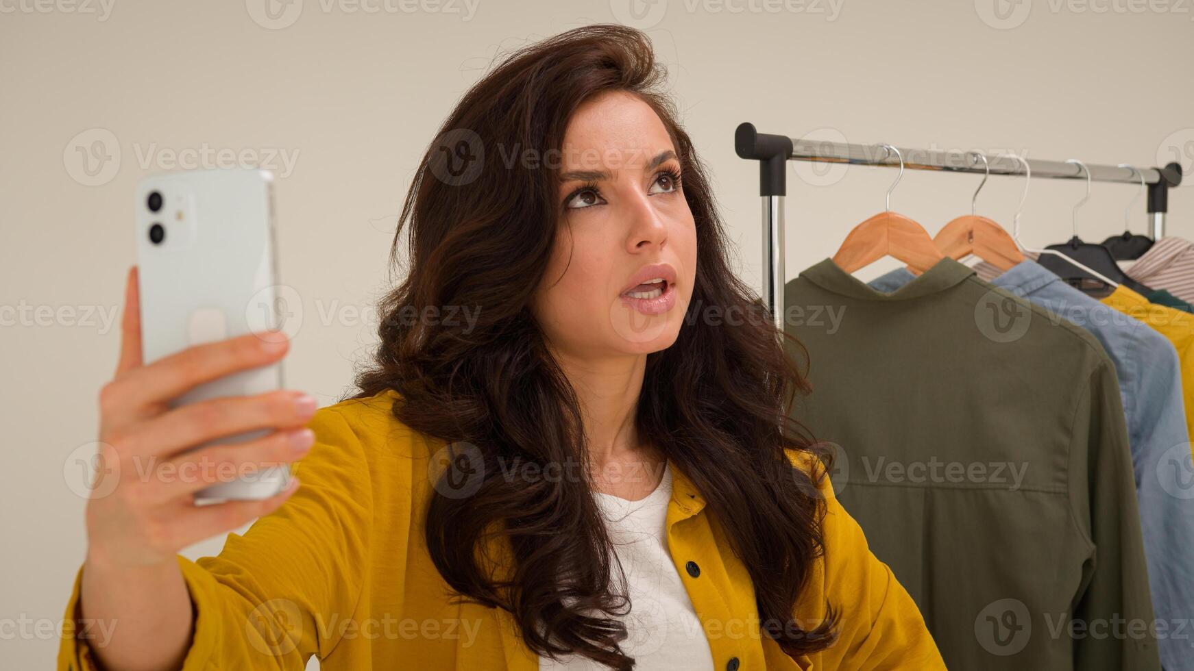 Displeased Caucasian woman female influencer vlogger streaming shoot blog broadcast use mobile phone annoyed blogger girl show shirt talk filming fashion review dissatisfied with clothes studio photo