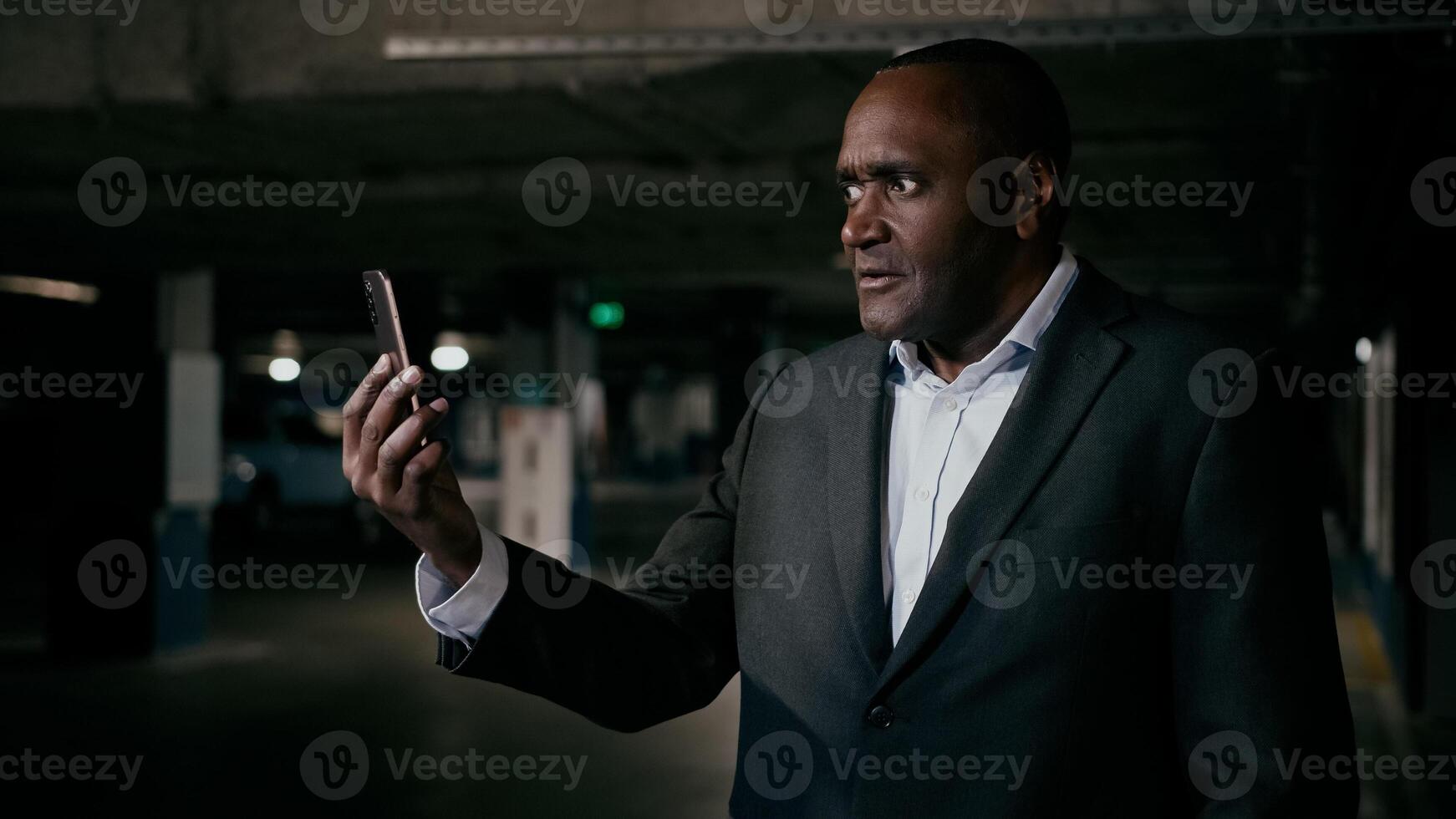 Upset puzzled dissatisfied african american man customer stressed male businessman speaking talking on call using cell phone in underground parking lot solve problem remote at online conference photo