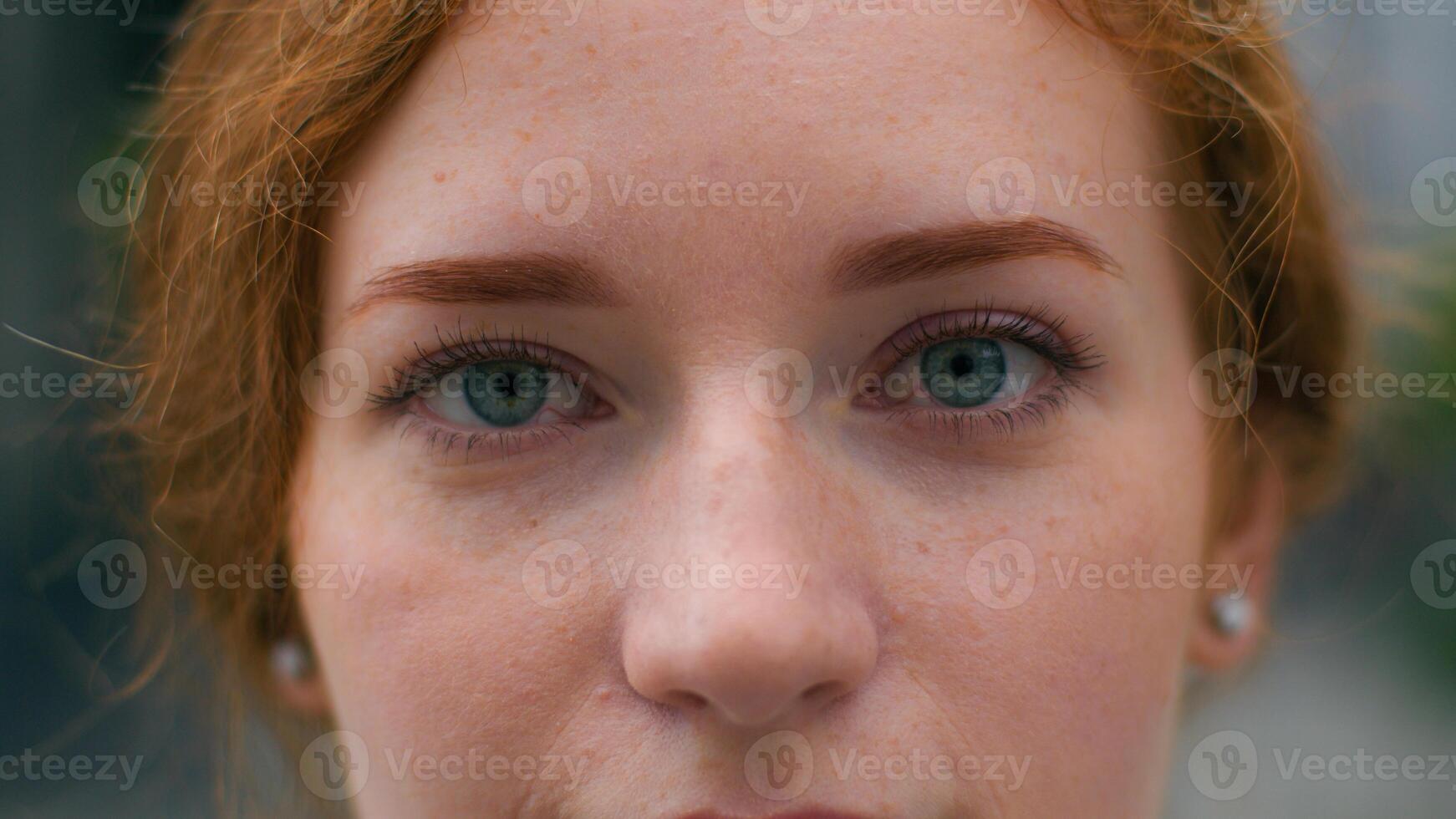 Close up beautiful smiling young Caucasian ginger woman face female lady girl slowly wide opening bright blue eyes looking camera outside city urban street. Clear vision makeup eyesight ophthalmology photo