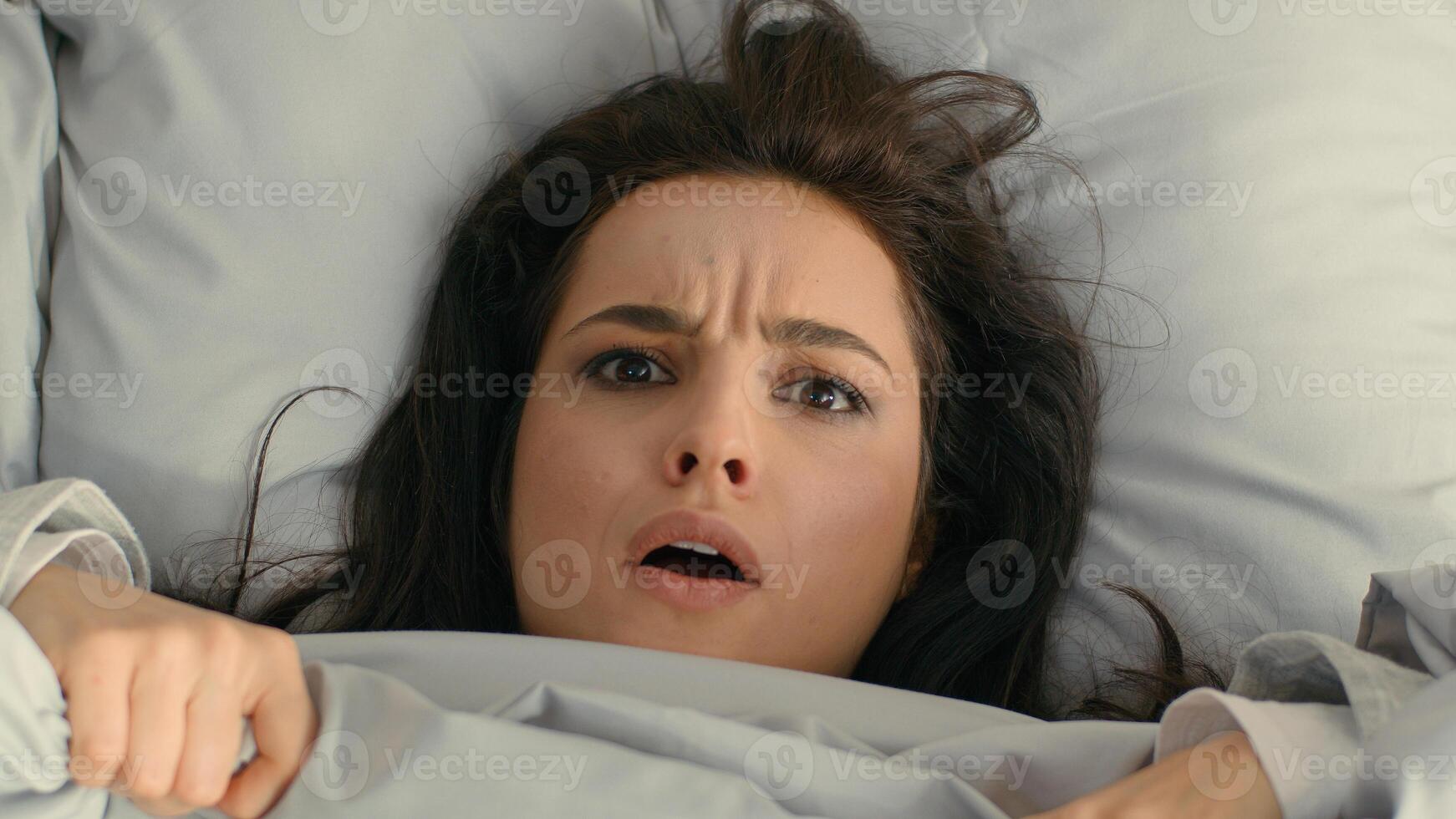 Close up woman unhappy girl female looking duvet blanket open mouth frowning face surprised bed home sleepy lazy peek out dissatisfied expression discomfort morning annoyed displeased asleep bedroom photo