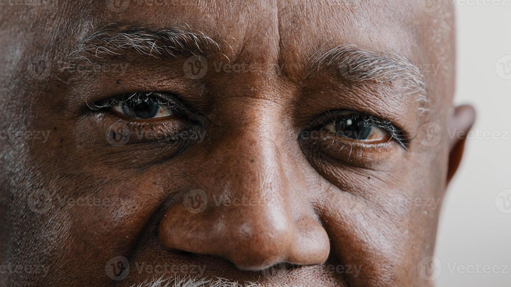Macro extreme close up half part of face elderly middle-aged African old wrinkled man with dark eyes sad calm mature male senior citizen looking at camera myopia vision sight problem poor eyesight photo