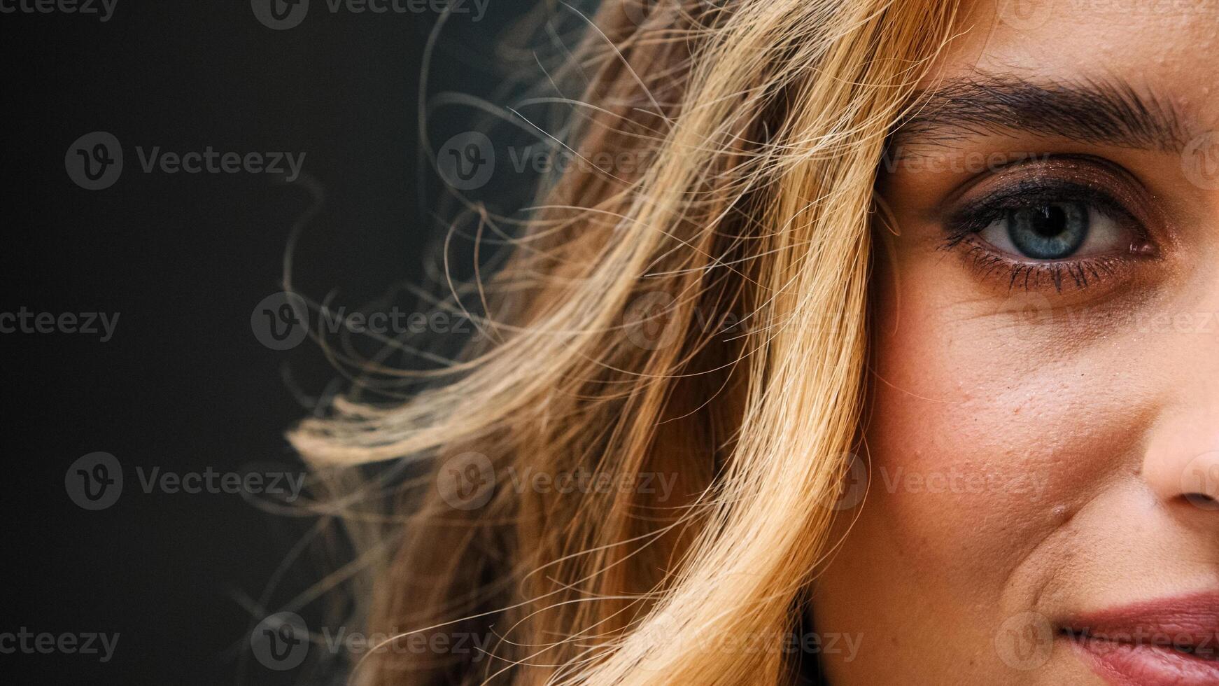 Close-up one blue female eye looks at camera with gaze with beautiful make-up. Half face young caucasian woman. Lady enjoys good eyesight vision laser correction uses contact lenses windy outdoors photo