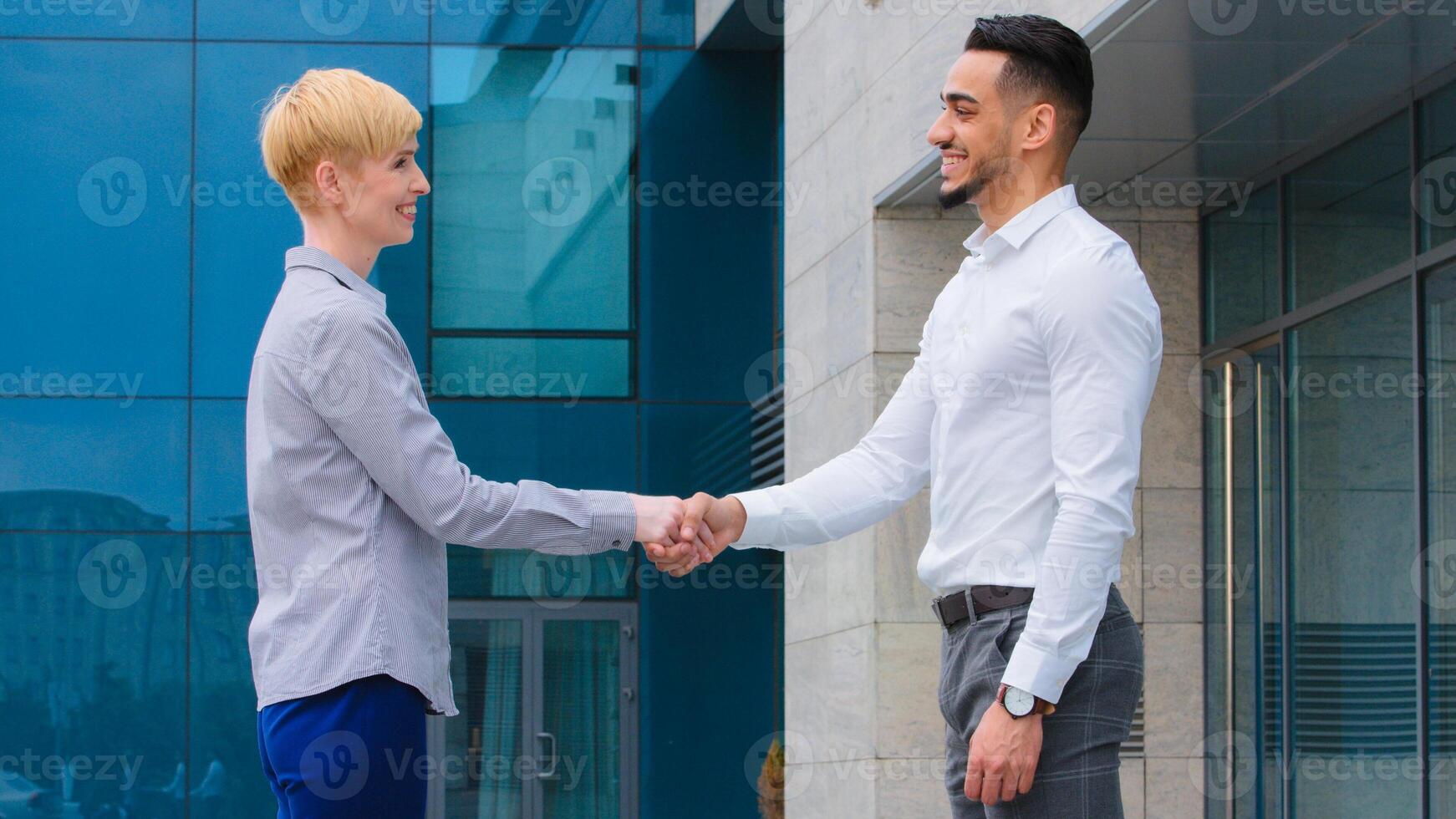 Two multiethnic colleagues arabic man and caucasian woman business partners stand outdoors near company building talking shake hands conclude deal union agreement handshake teamwork goodbye gesture photo