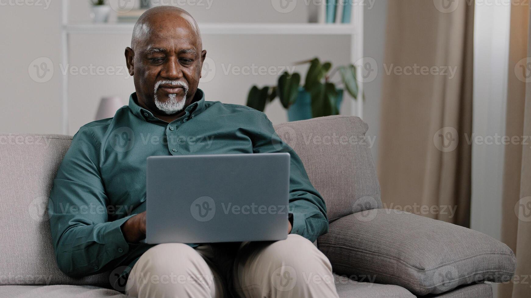African American bald bearded businessman teacher writer entrepreneur checking data online use computer application connection wifi network at home office sitting on comfortable sofa typing on laptop photo