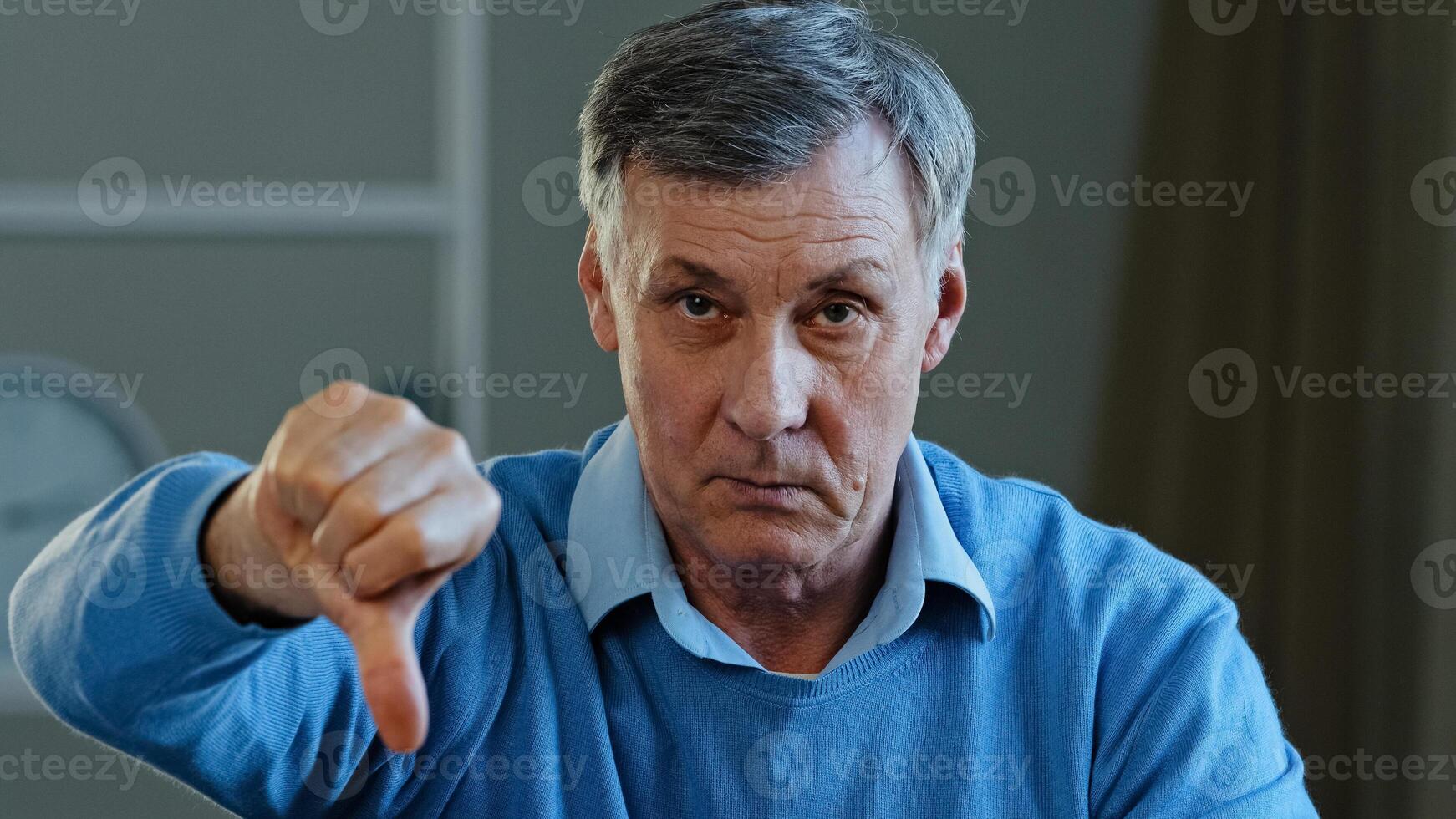 Portrait of upset angry sad elderly man looking at camera disgruntled serious mature old grandpa showing dislike thumbs down negative attitude disapproval gesture bad assessment disagreement low mark photo