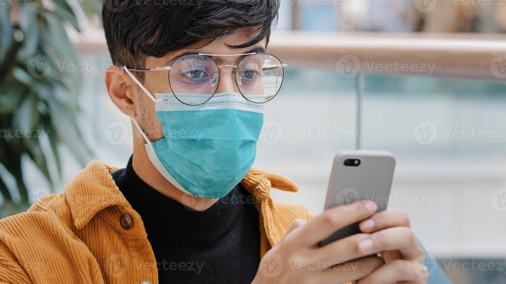 Close-up young arab guy in protective mask typing message on smartphone using mobile application chatting social network writing sms making online order from phone browsing web enjoying modern tech photo
