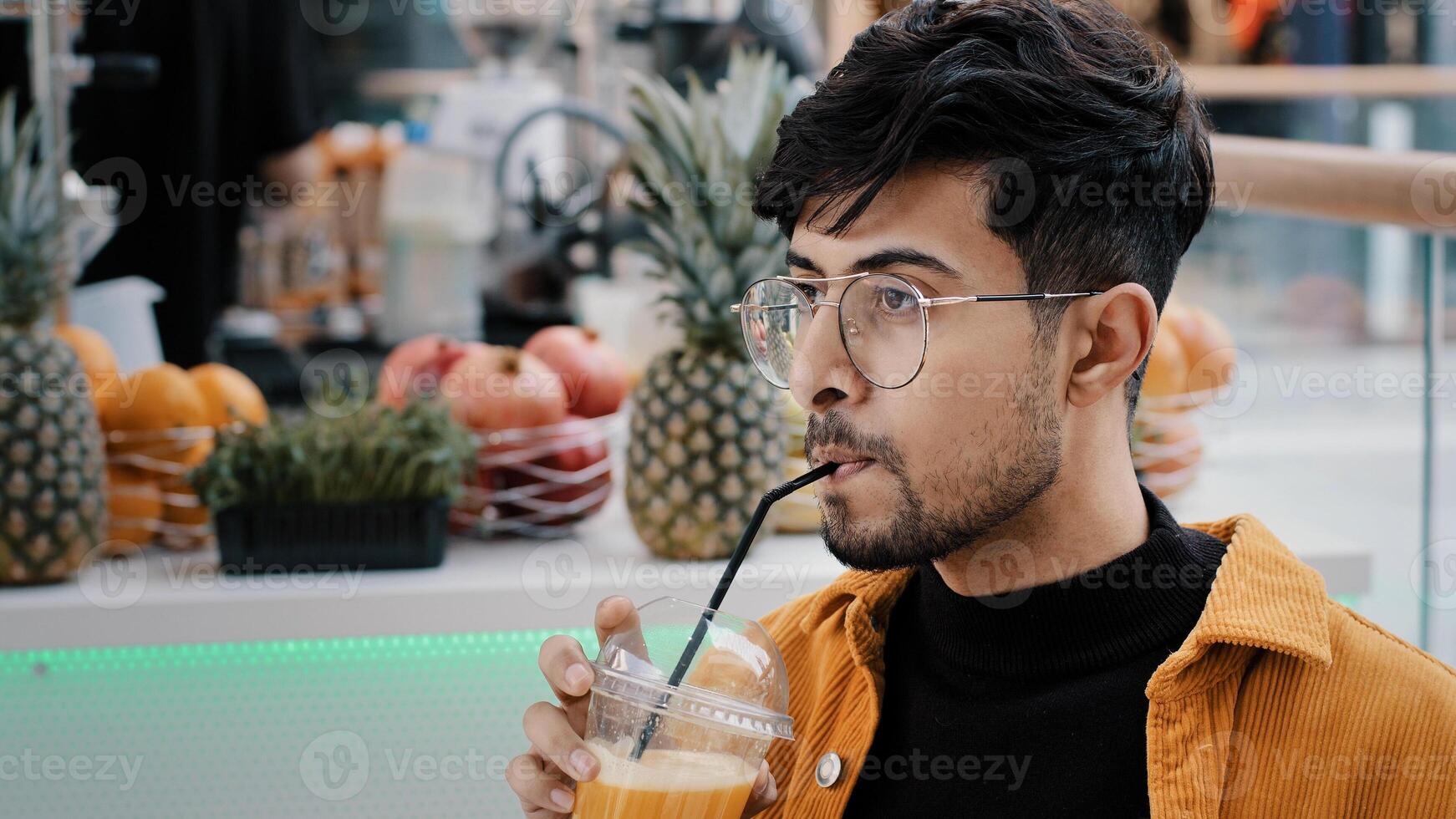 Young hispanic male cafe client resting spending weekend drinking exotic drink from plastic disposable cup relaxing happy carefree guy enjoying taste refreshing fruit juice looking at camera smiling photo