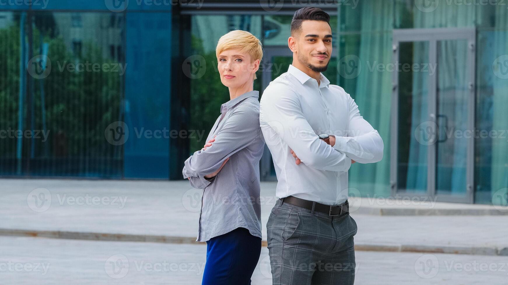Hispanic business man lawyer manager and caucasian beautiful businesswoman secretary short haired woman entrepreneurs wearing formal clothes posing standing outdoors crossing arms looking at camera photo