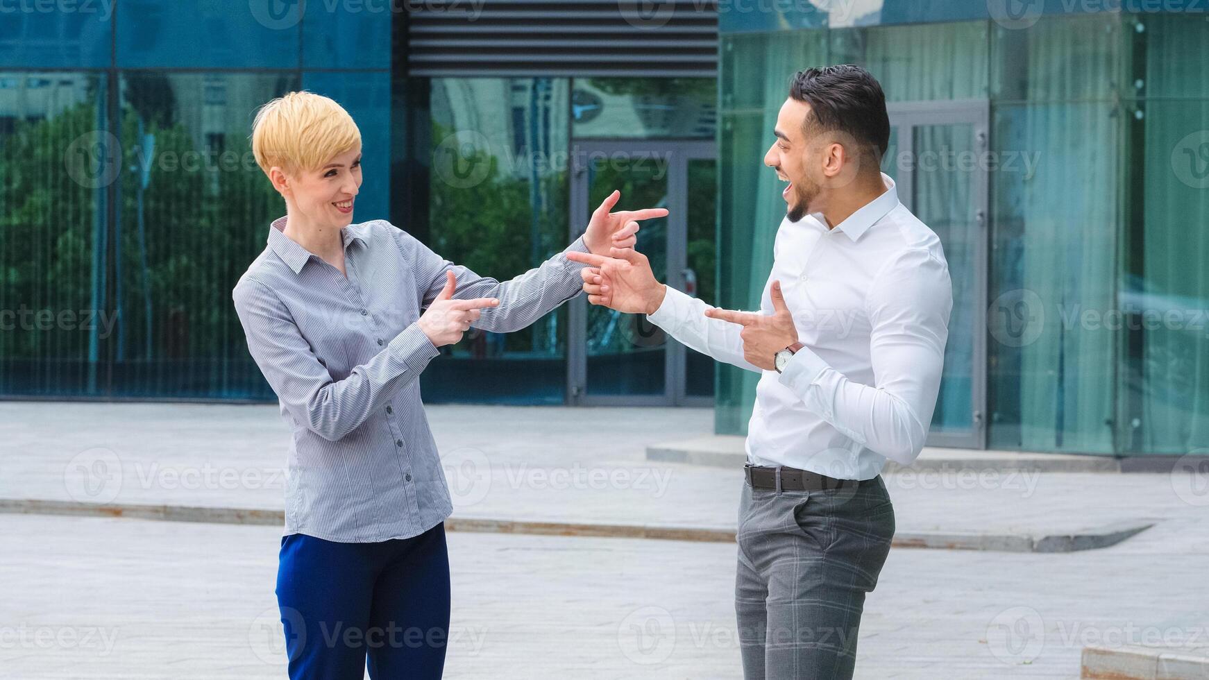Multiracial couple business colleagues arabic spaniard man manager boss and caucasian adult blonde woman standing outdoors talking actively gesturing hands gesture hey you pretend to shoot fingers photo