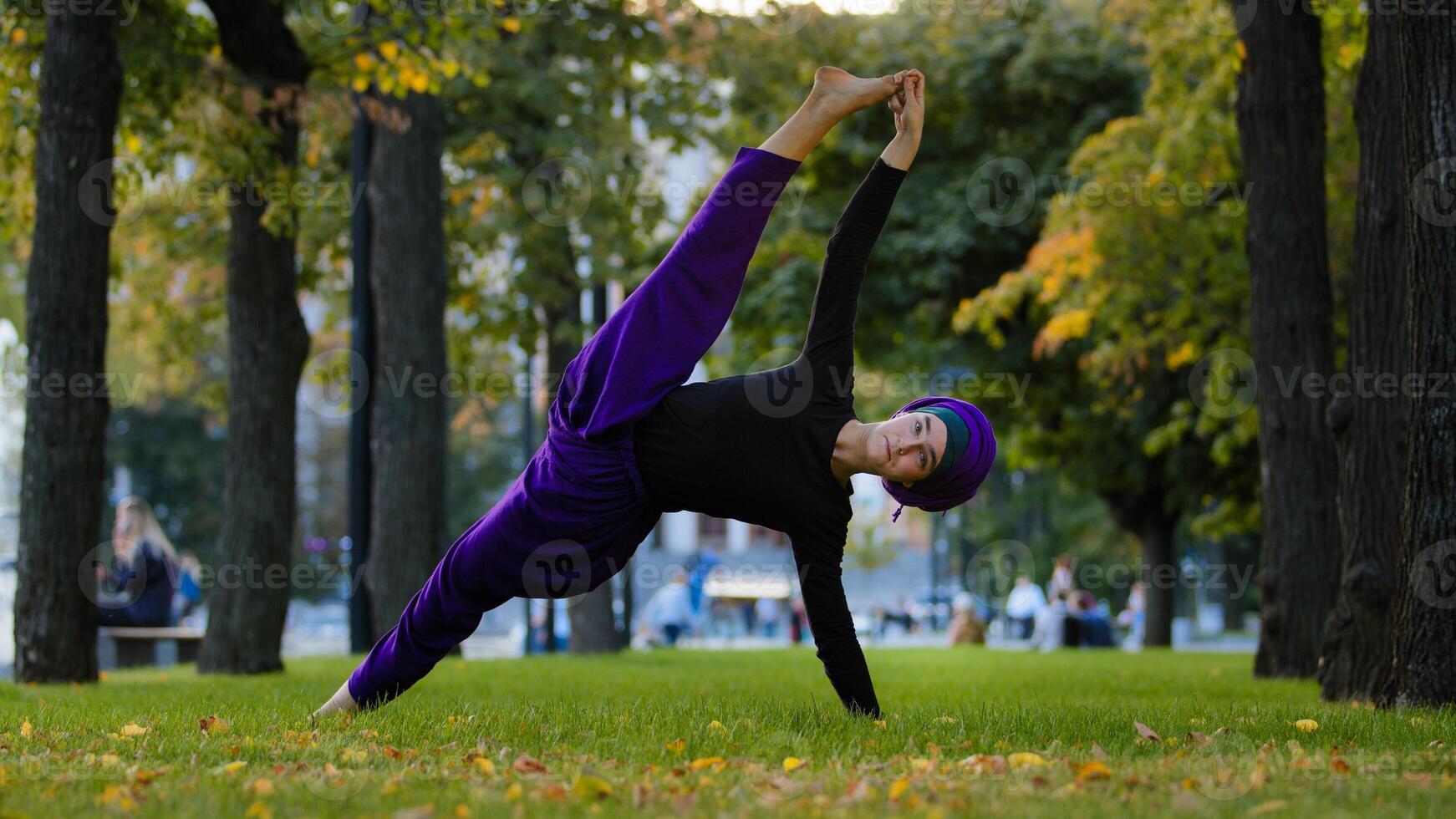Strong sportive islamic girl in hijab yoga teacher woman stands in side plank on grass in park doing Ardhachandrasana Vasishthasana asana pose, exercising outdoors workout standing, good stretching photo