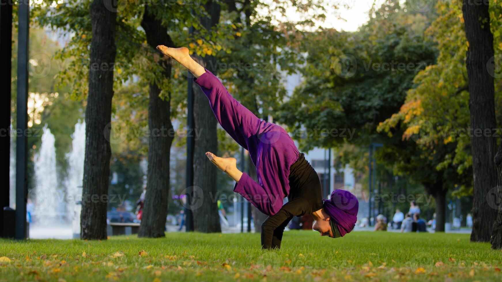 Strong active muslim girl in hijab woman yogi sportswoman doing yoga workout in park on green lawn doing balance handstand training holding leg in air acrobatic element moves actively stretching asana photo