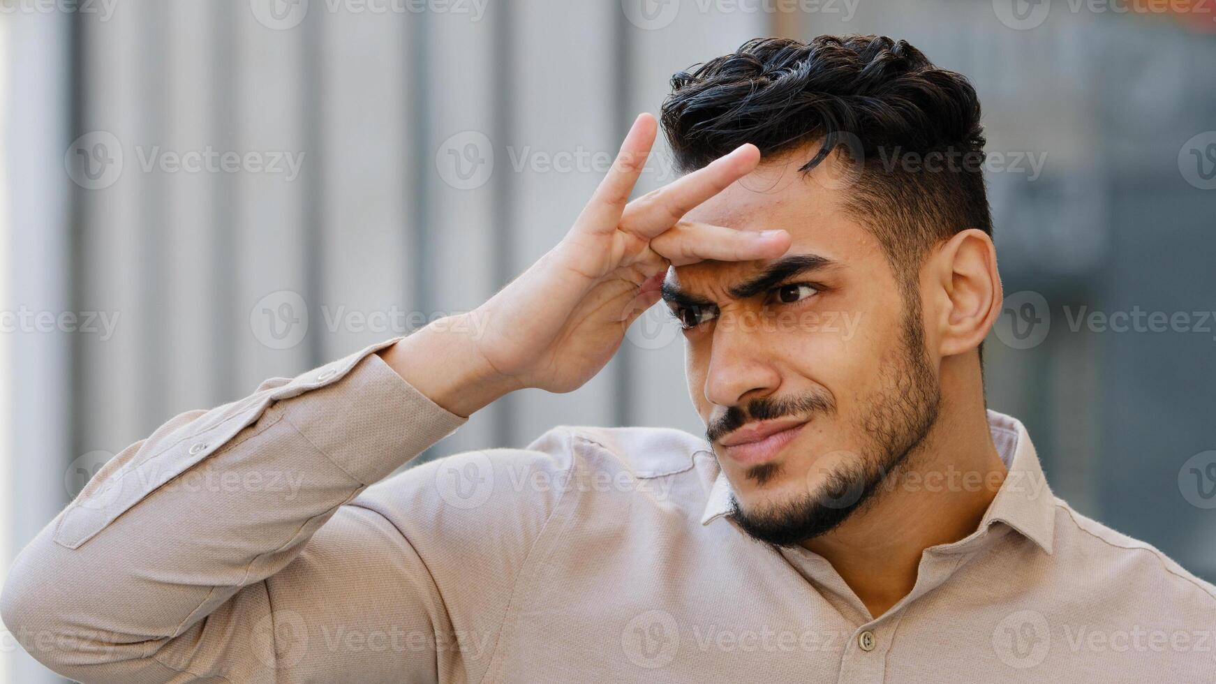 Close-up male suspicious face portrait outdoors in city spy bearded guy funny man looking into distance searching holding hands near forehead peeking out someone waiting looks around choosing search photo