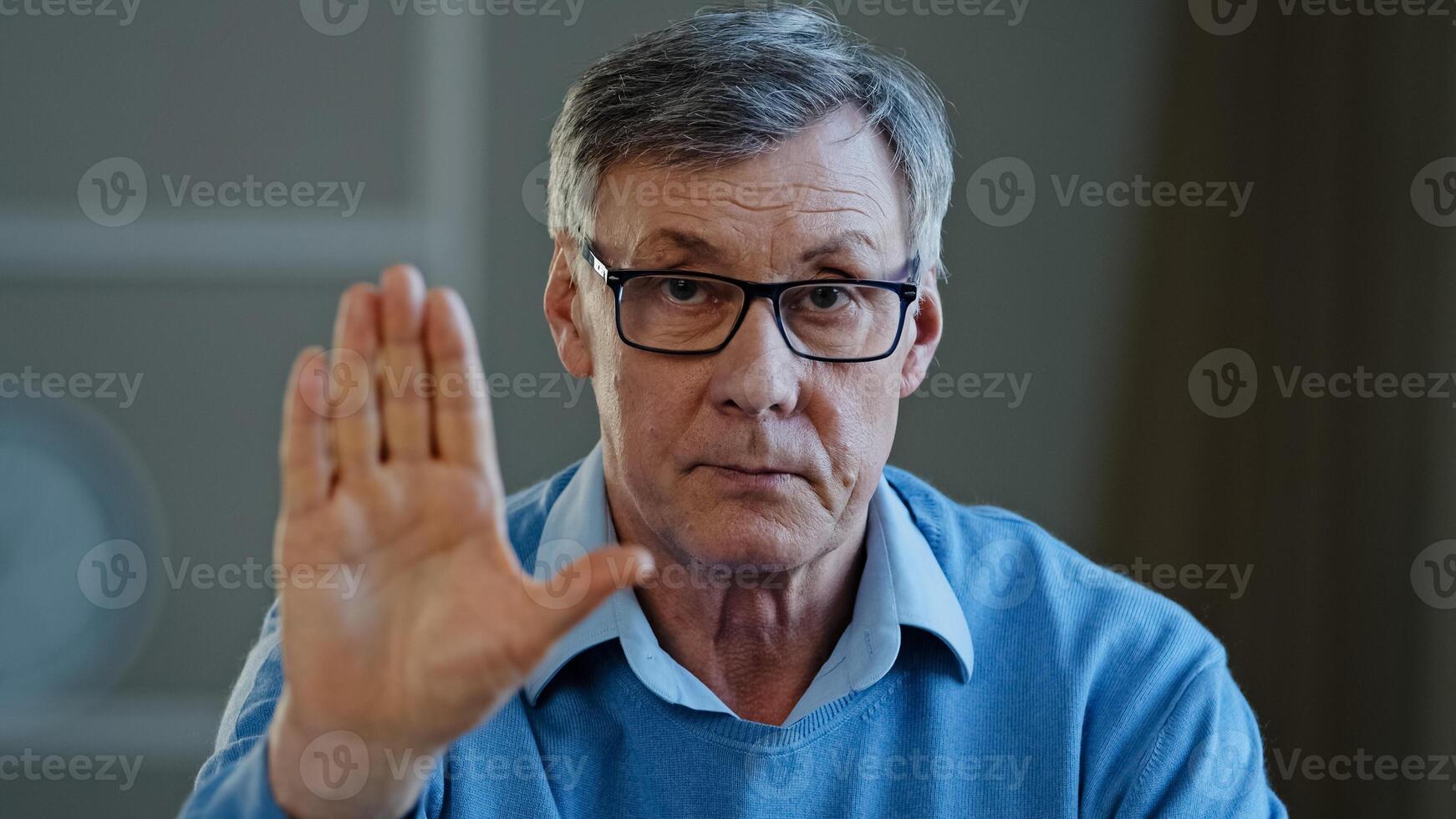 Serious old senior mature 60s man stretch out palm to camera says stop gesture indoors. Social problems older generation disrespect ban refusal disagreement. Aged businessman trouble denial rejection photo