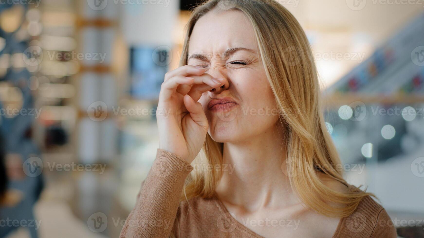 Portrait young caucasian woman with rhinitis runny nasal virus illness sneezes wipes with paper napkin in shopping mall student girl suffer from seasonal allergy dusty nose irritation disease symptoms photo