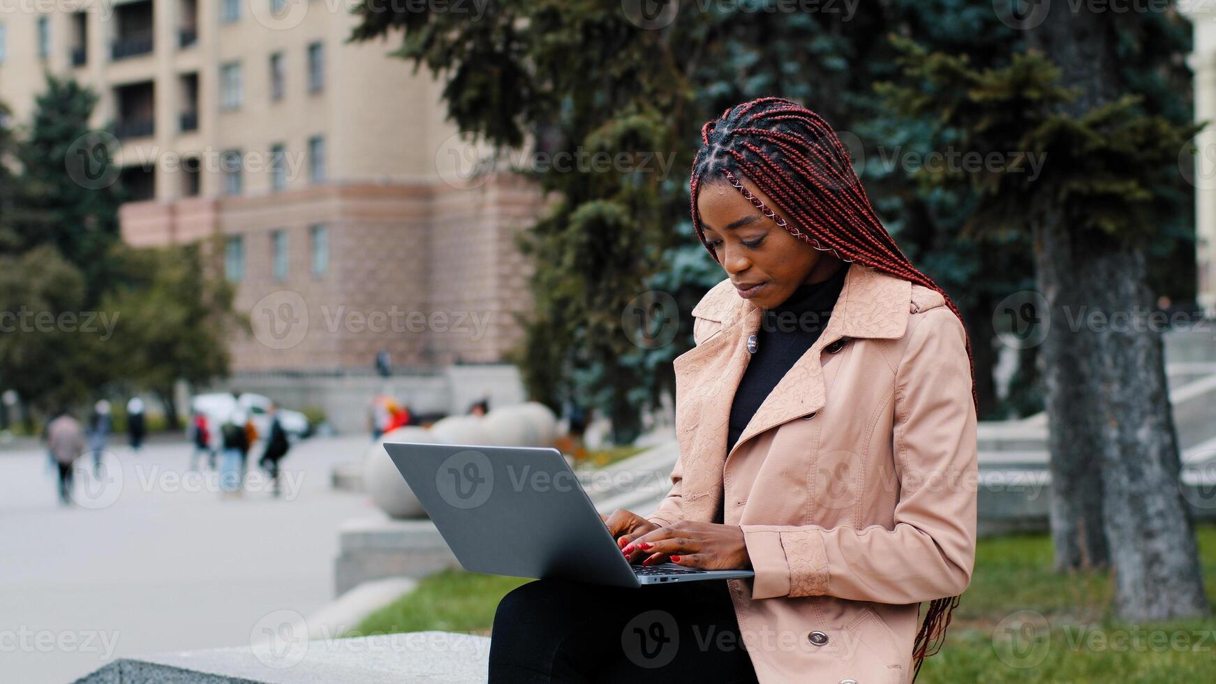 Serious african american girl blogger using laptop, sitting outdoor, young busy focused businesswoman looking at screen, intern typing on keyboard, writing report, student working on research project photo