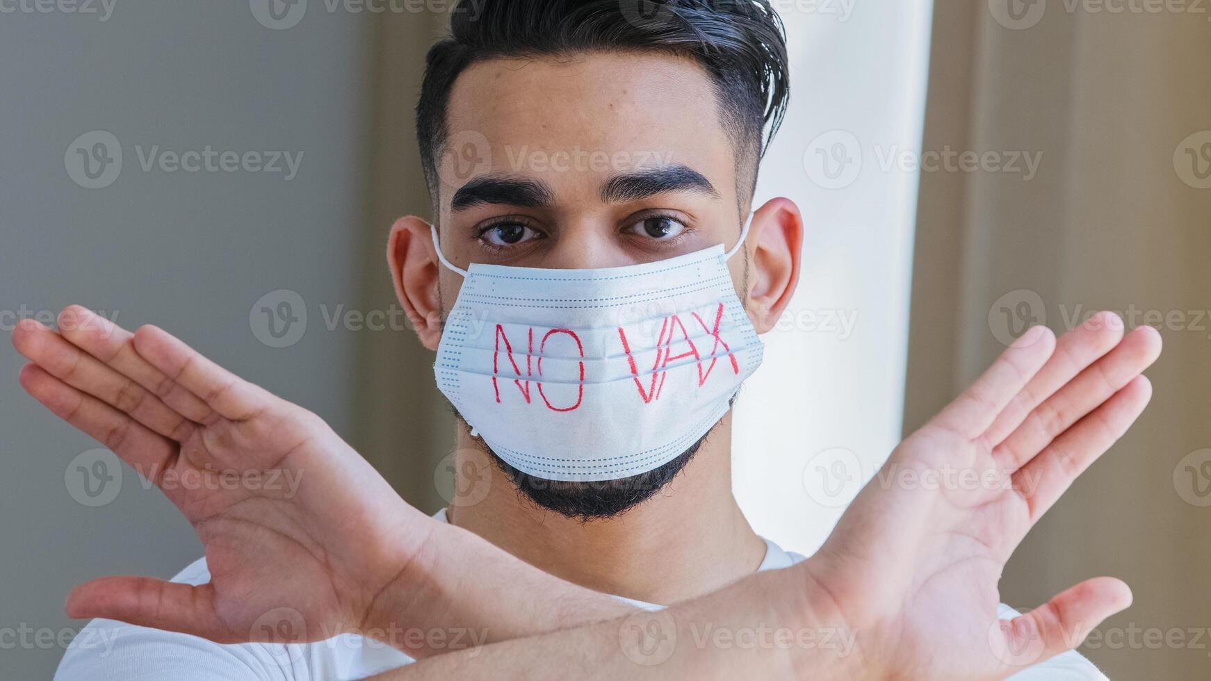 Portrait of arab hispanic man in medical protective mask with inscription no vaccine crosses arms in front of him refusing demonstrating protest refusal to be vaccinated against covid coronavirus flu photo