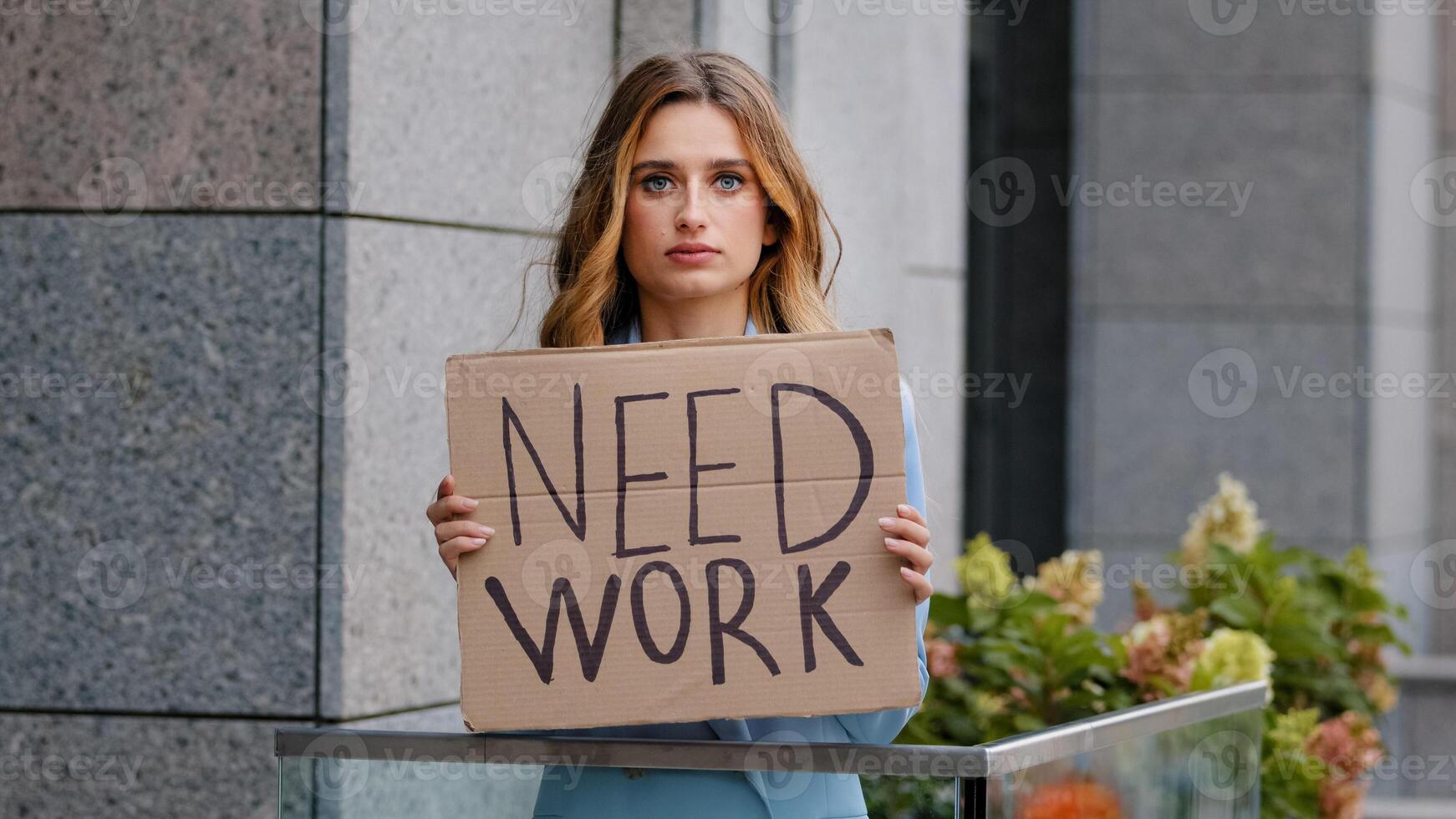 Sad unemployed blonde business woman stands in city looking at camera holds cardboard banner needs work job worried problems with finances. Career loss. Unemployment pandemic crisis. Poor girl fired photo
