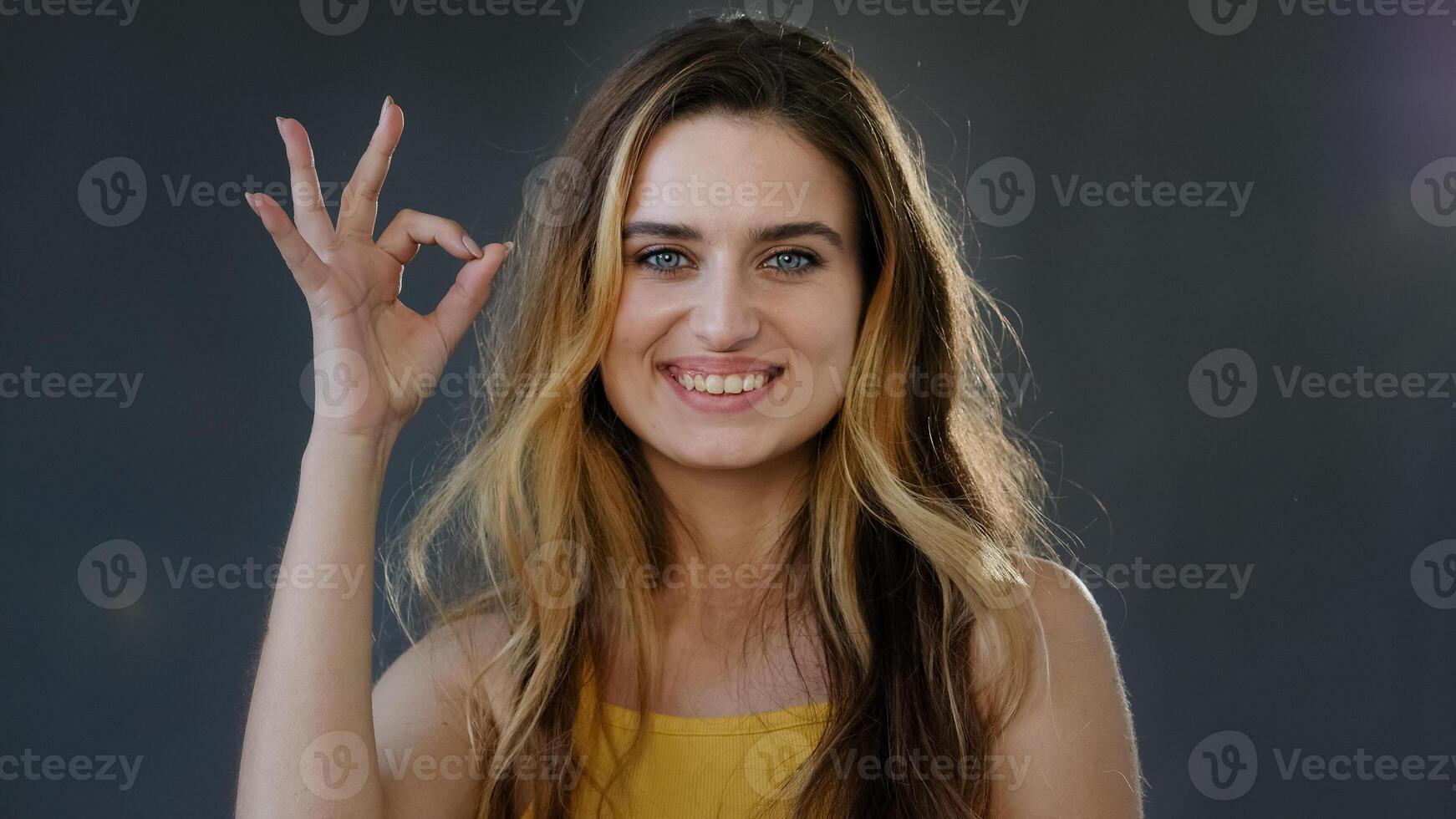 Female portrait successful feminist woman millennial girl lady blonde model shows ok sign symbol everything okay well good perfect gesture smiling looking at camera standing on gray studio background photo