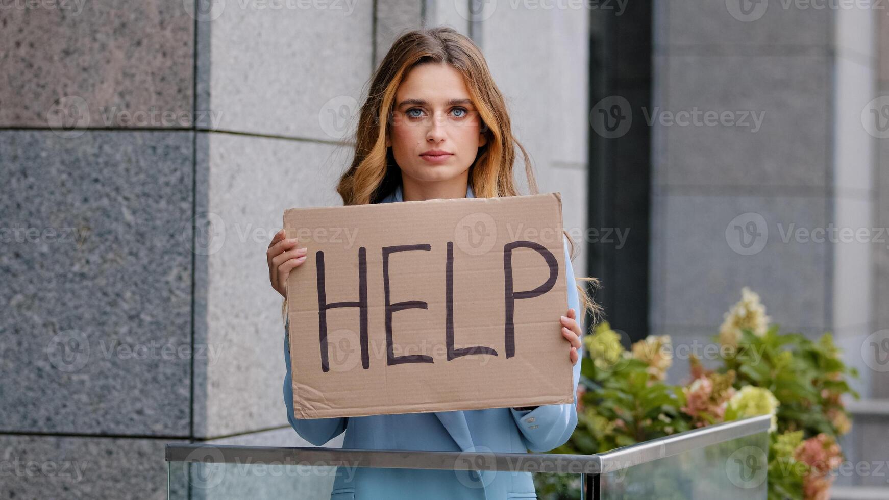 Portrait sad fired poor caucasian millennial business woman standing in city looking at camera holding cardboard sign banner text help asks for work rescue worries about unemployment problem crisis photo