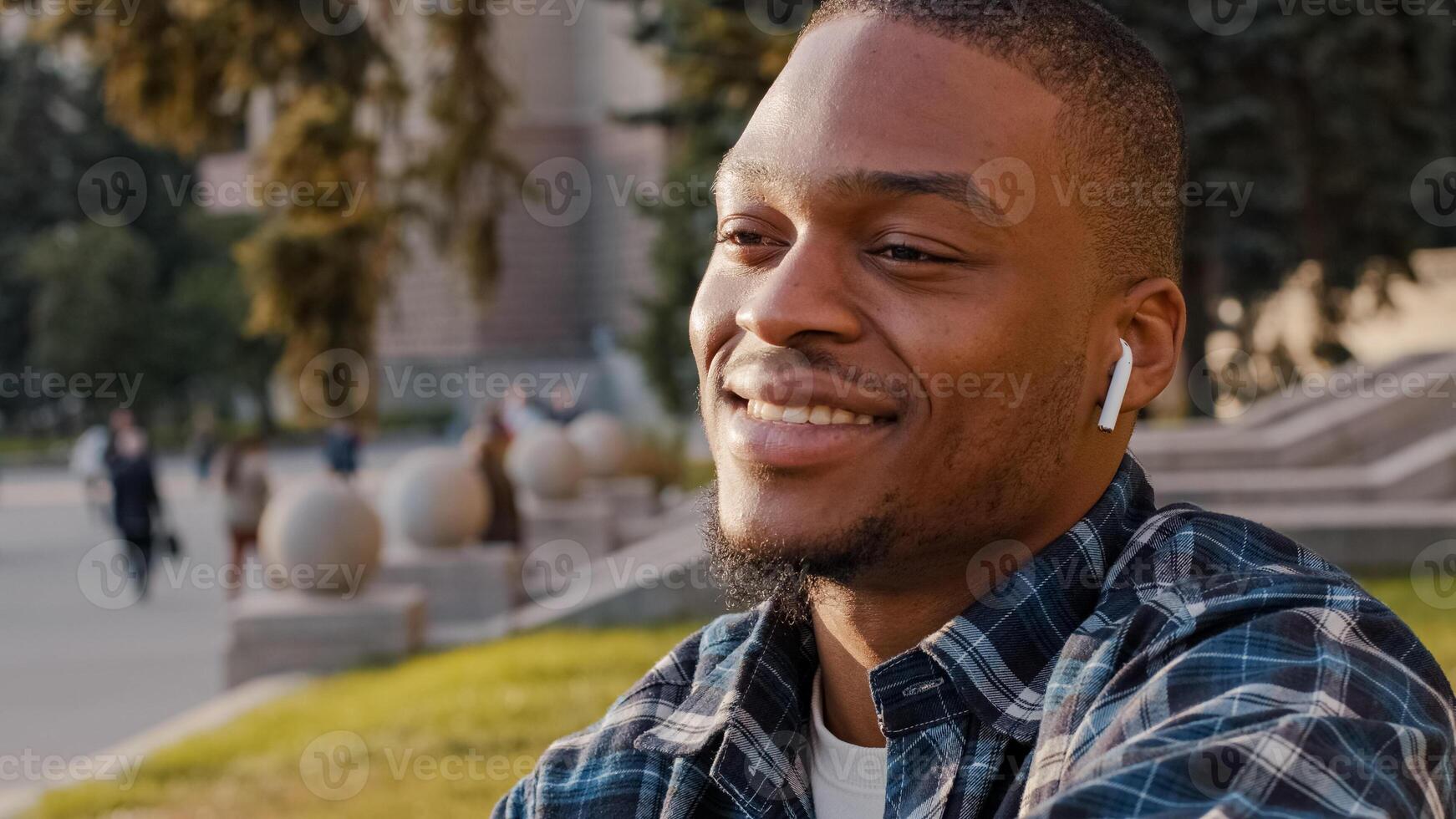African american handsome young man listening music wireless headphones in city town center. Close up portrait multiracial guy student enjoying song audio sound with earphones smiling outdoors photo