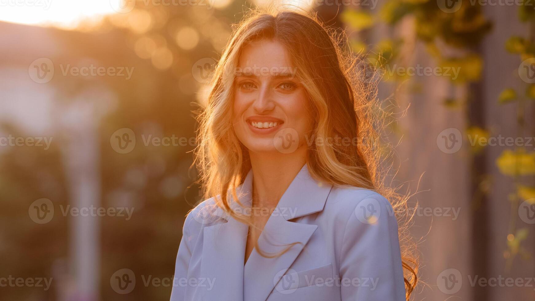 Portrait pleased happy Caucasian blonde girl with long hair stands sun rays background looking at camera smiling sincerely toothy with white teeth. Millennial girl posing in sunlight with smile photo