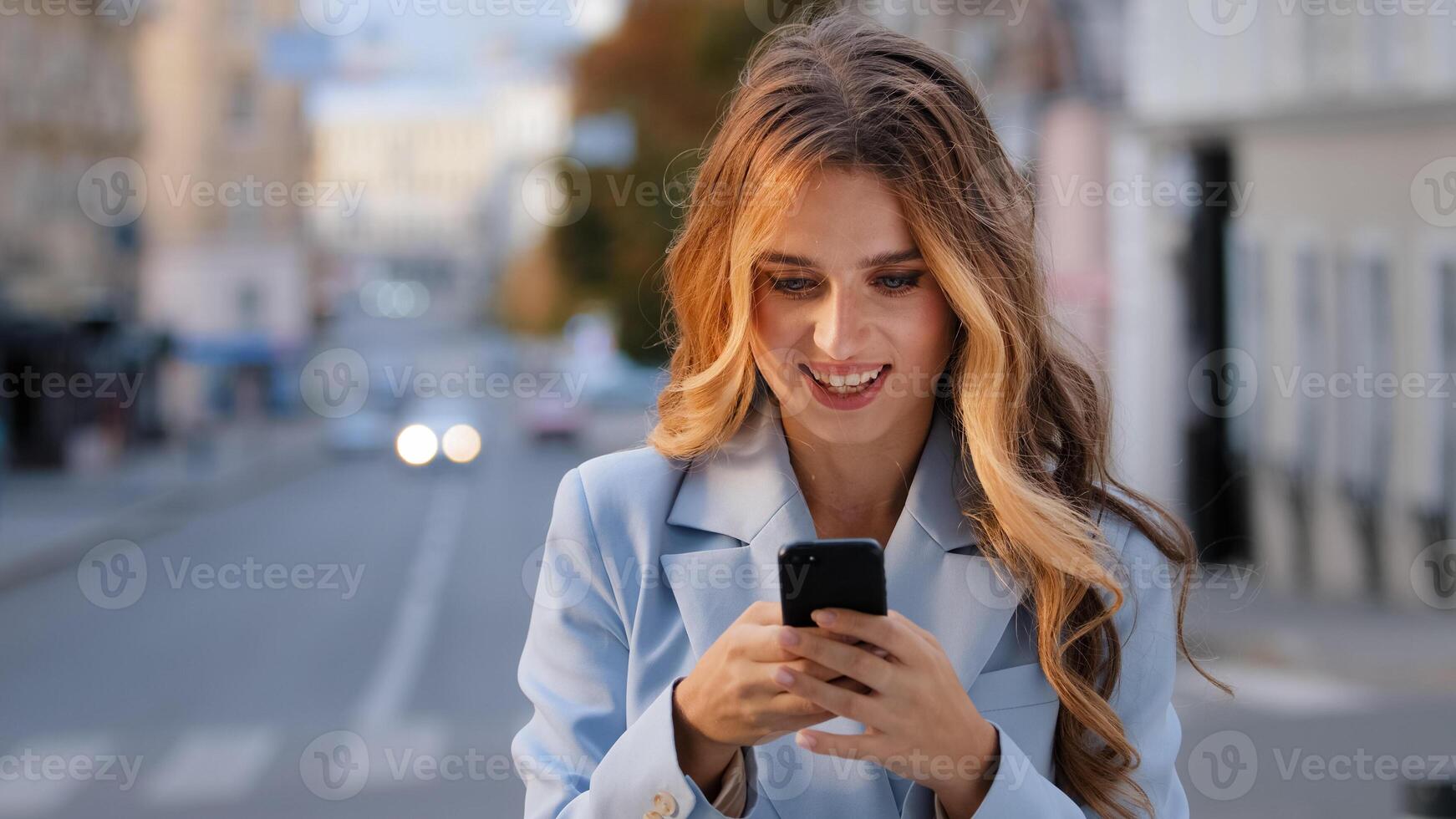 Portrait caucasian girl business woman looking into mobile phone rejoices victory good news chatting in net receives message from boyfriend successful e-commerce buying online standing on city photo