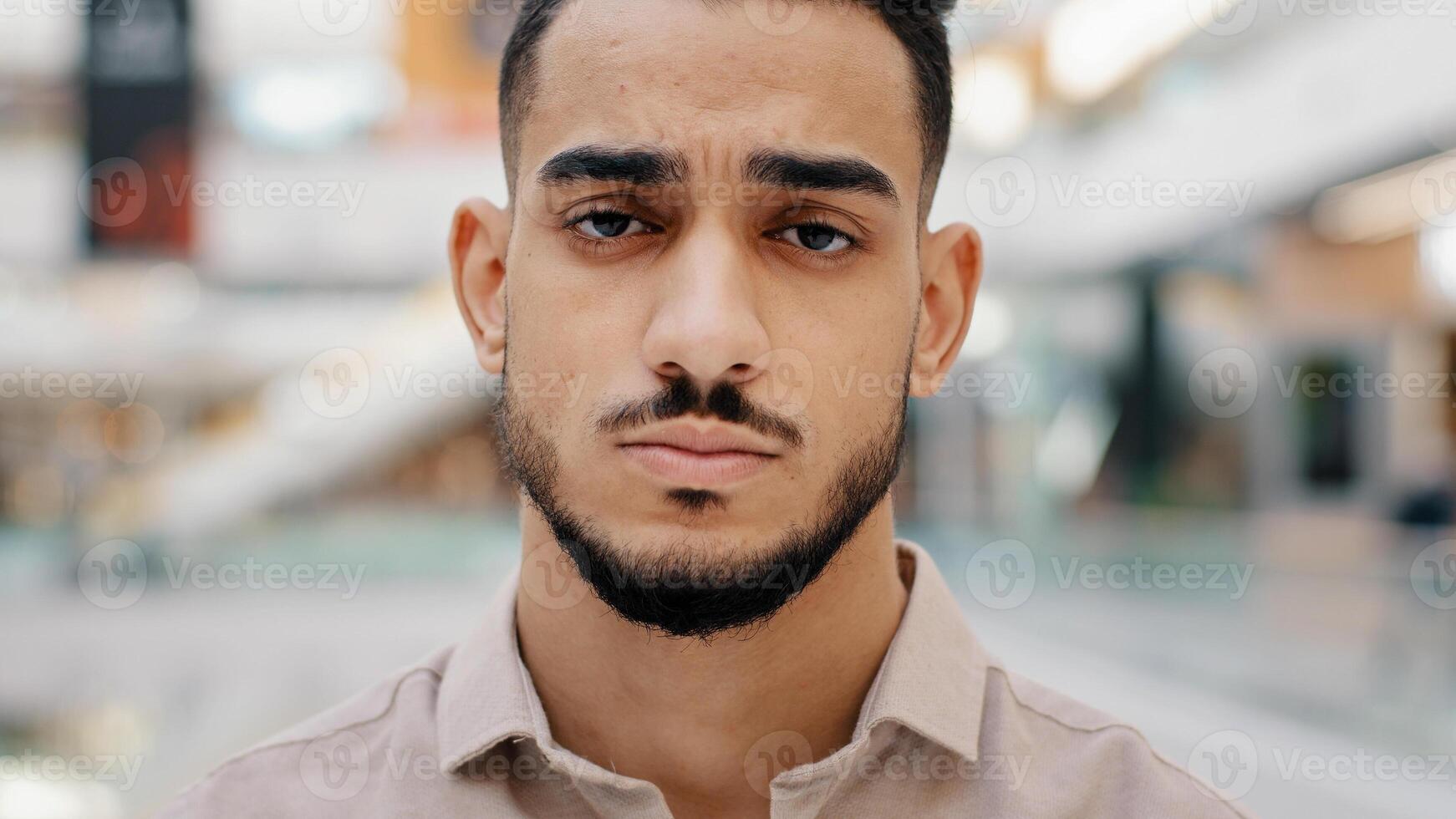 Close-up of face upset young man sad frustrated millennial guy looking at camera serious hispanic male having negative thoughts depressive mood difficult period life misunderstanding problems at work photo