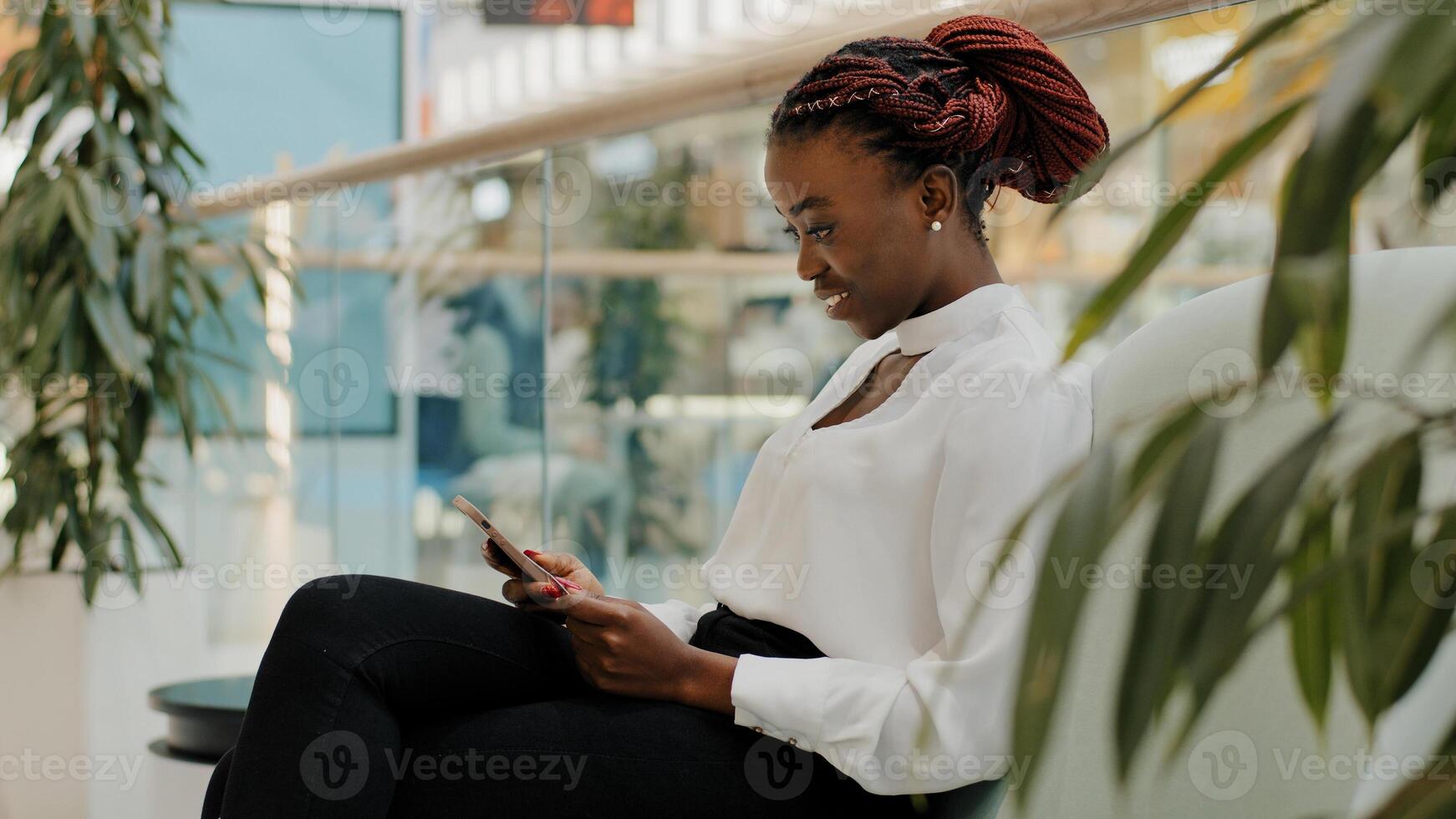 Happy business woman african american girl worker manager young female sitting in corridor office modern creative company in shopping center chatting in mobile phone using smartphone online browsing photo