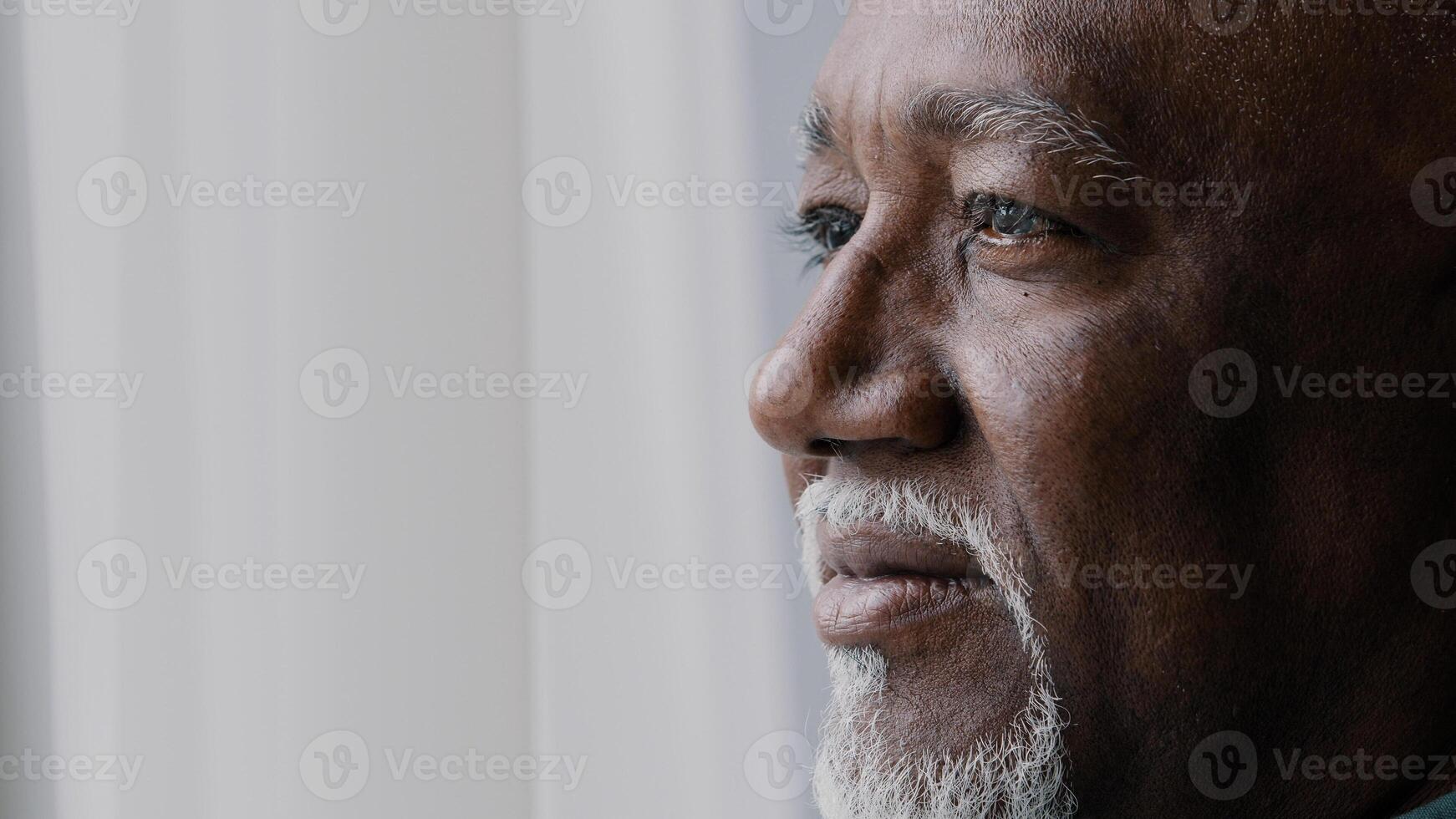 Close up pensive male old wrinkled face, 60s African bearded man deep in sad thoughts looking at window, elderly grandfather look away think about disability feel lonely. Nostalgia retired businessman photo