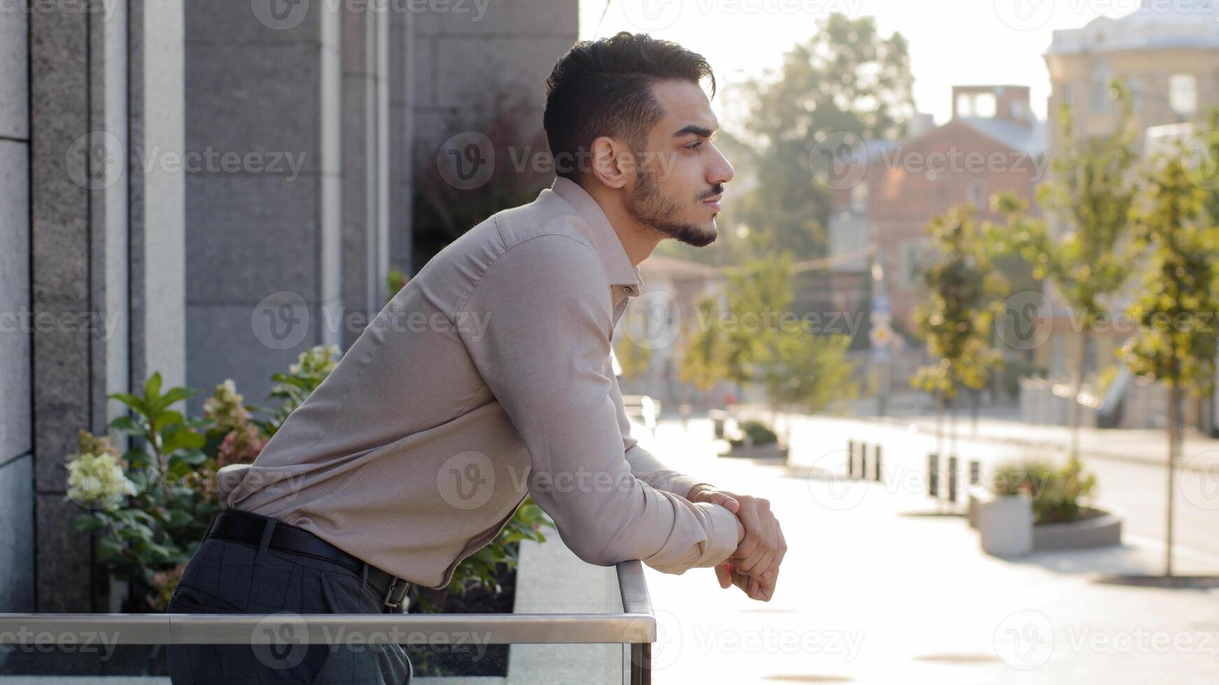Happy pensive successful relaxed business man hispanic guy male arabic investor businessman stands on terrace balcony in office building in hotel room at home thinking looking at cityscape enjoy view photo