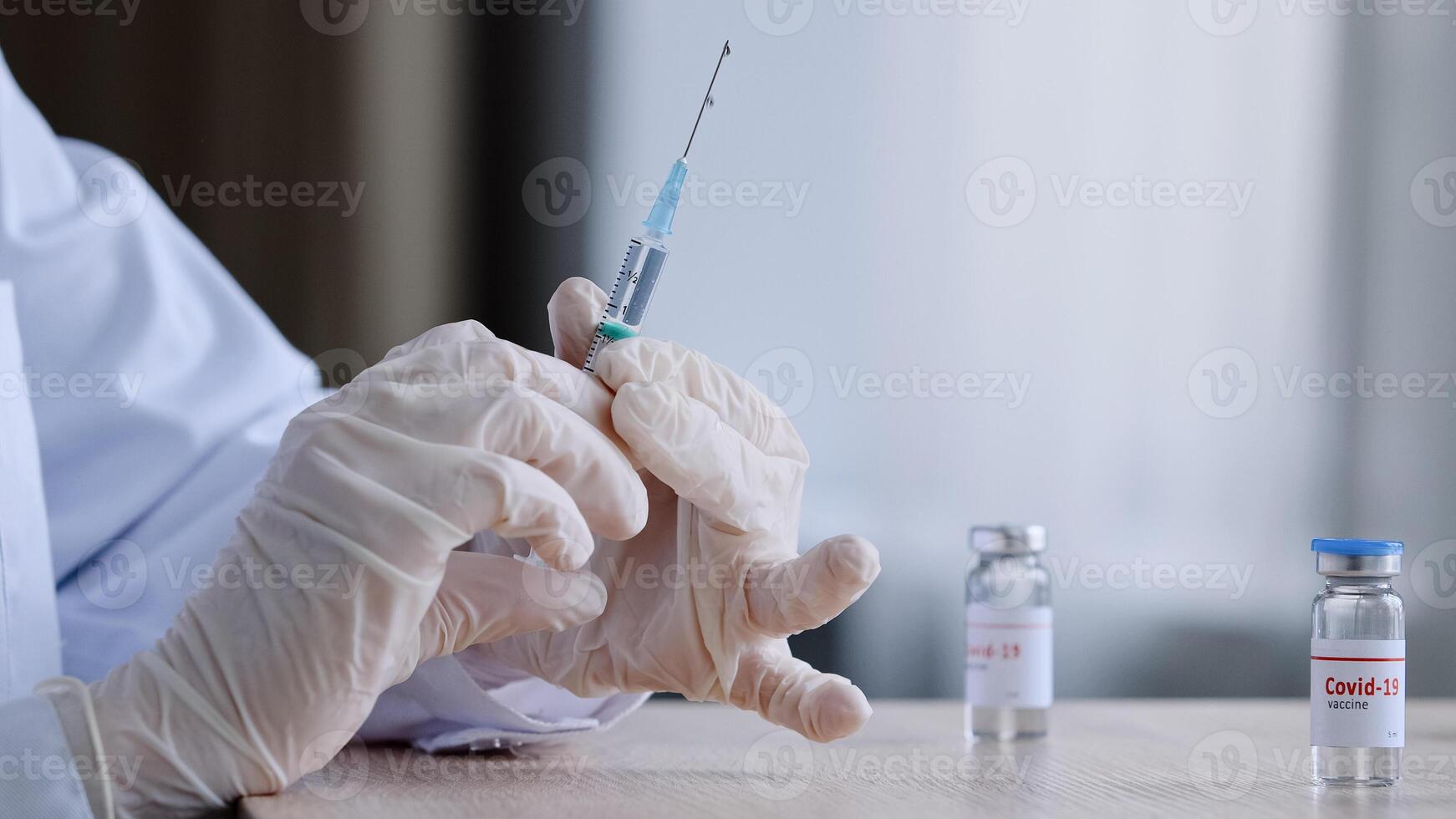 irreconocible médico enfermero médico trabajador en blanco Saco y látex guantes sostiene jeringuilla chapoteo medicina preparando para inyección sentado a mesa con dos botellas de vacuna enfermedad recurso, vacunación foto