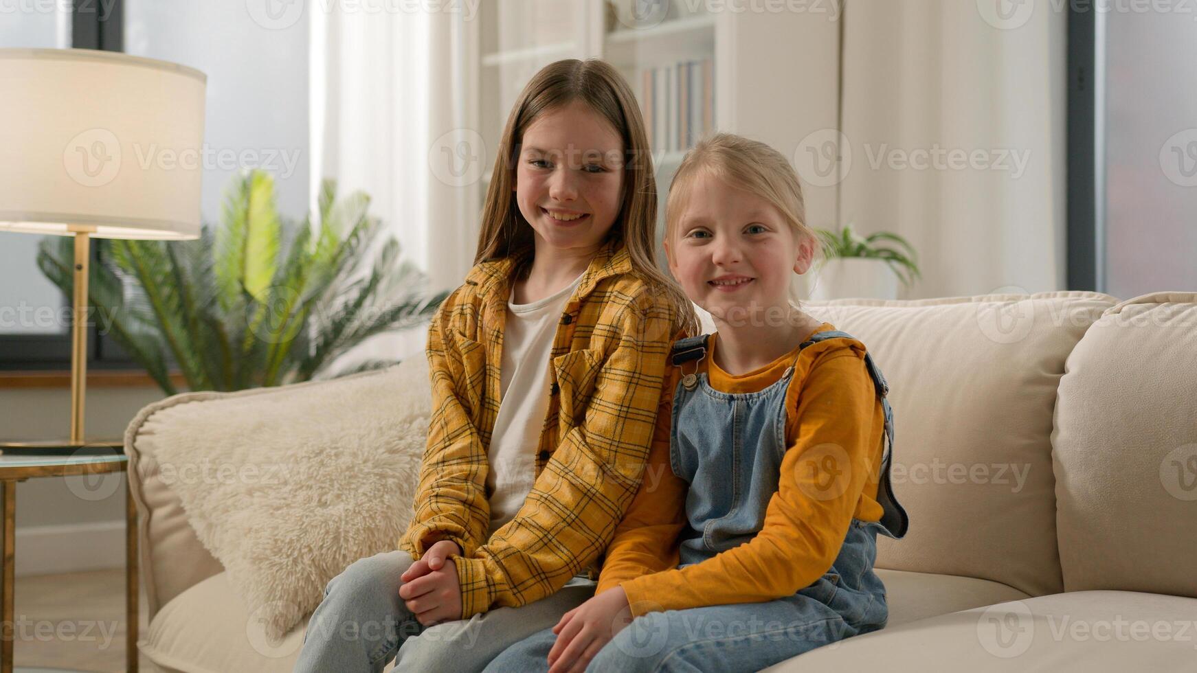 Two happy Caucasian children little girls daughters looking at camera together dental healthy toothy smile sisters kids friends posing relax showing positive emotion family couch living room indoors photo