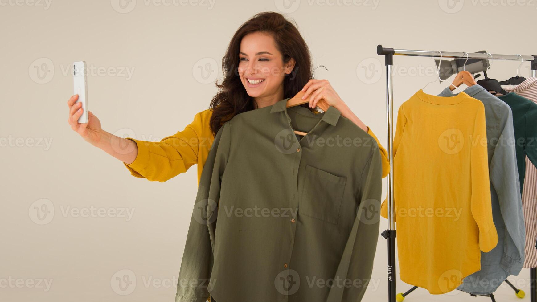 Smiling cheerful Caucasian woman female influencer blogger shooting blog wave hello mobile phone smartphone. Girl vlogger talk walk showing studio clothes streaming broadcast live online at home photo